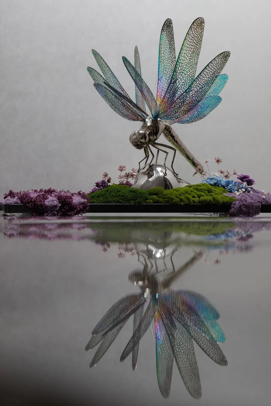 A metallic dragonfly sculpture adorned with colorful flowers and moss.