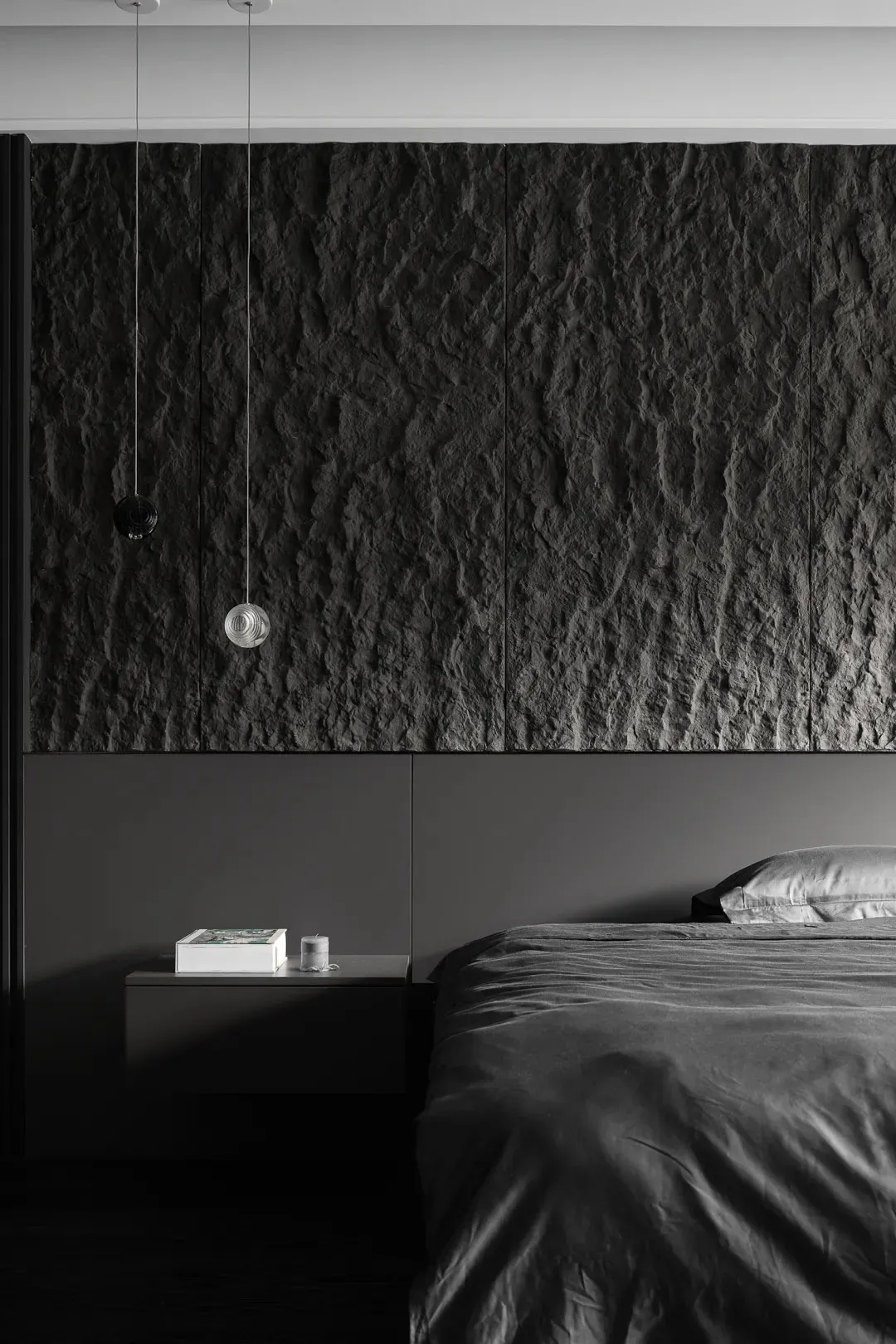 A minimalist bedroom featuring a dark stone accent wall and dark bedding.
