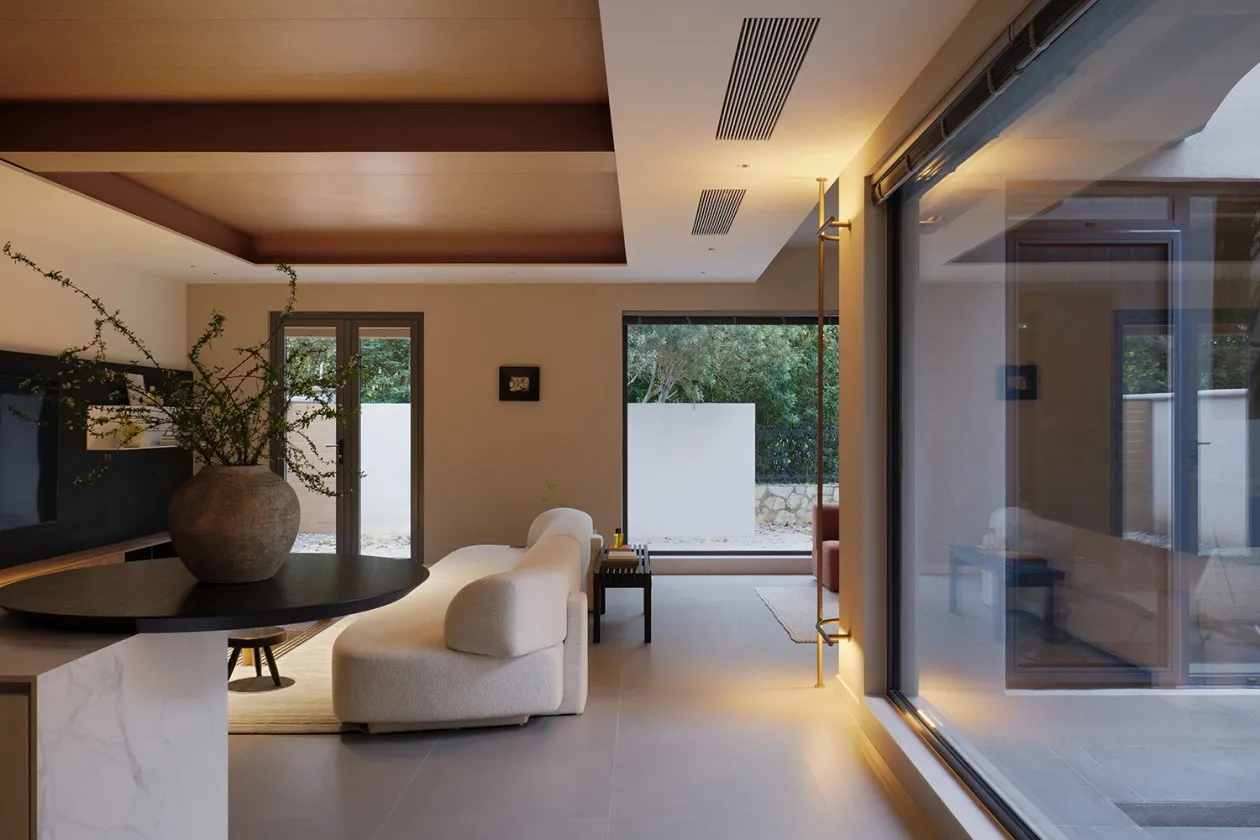 A minimalist living room with a neutral-color fabric sectional sofa, a round black coffee table, a large vase with greenery,