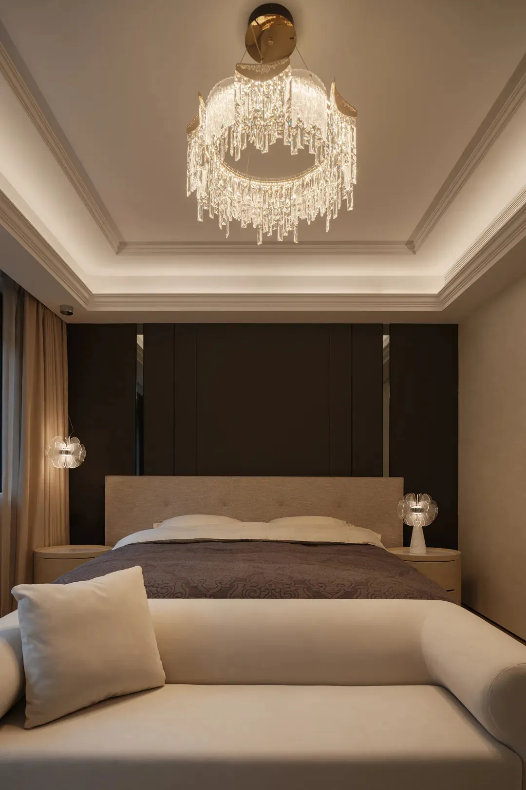 A modern bedroom featuring a bed with glass headboard and fabric bedding, illuminated by stylish pendant lights.