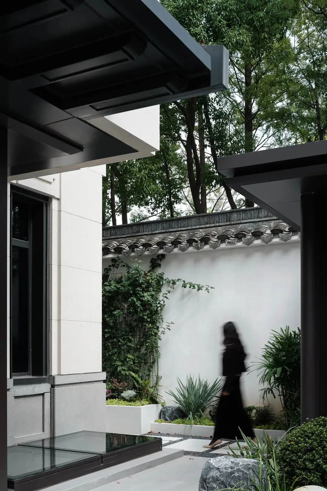 A modern exterior architectural design featuring concrete, glass, and greenery.