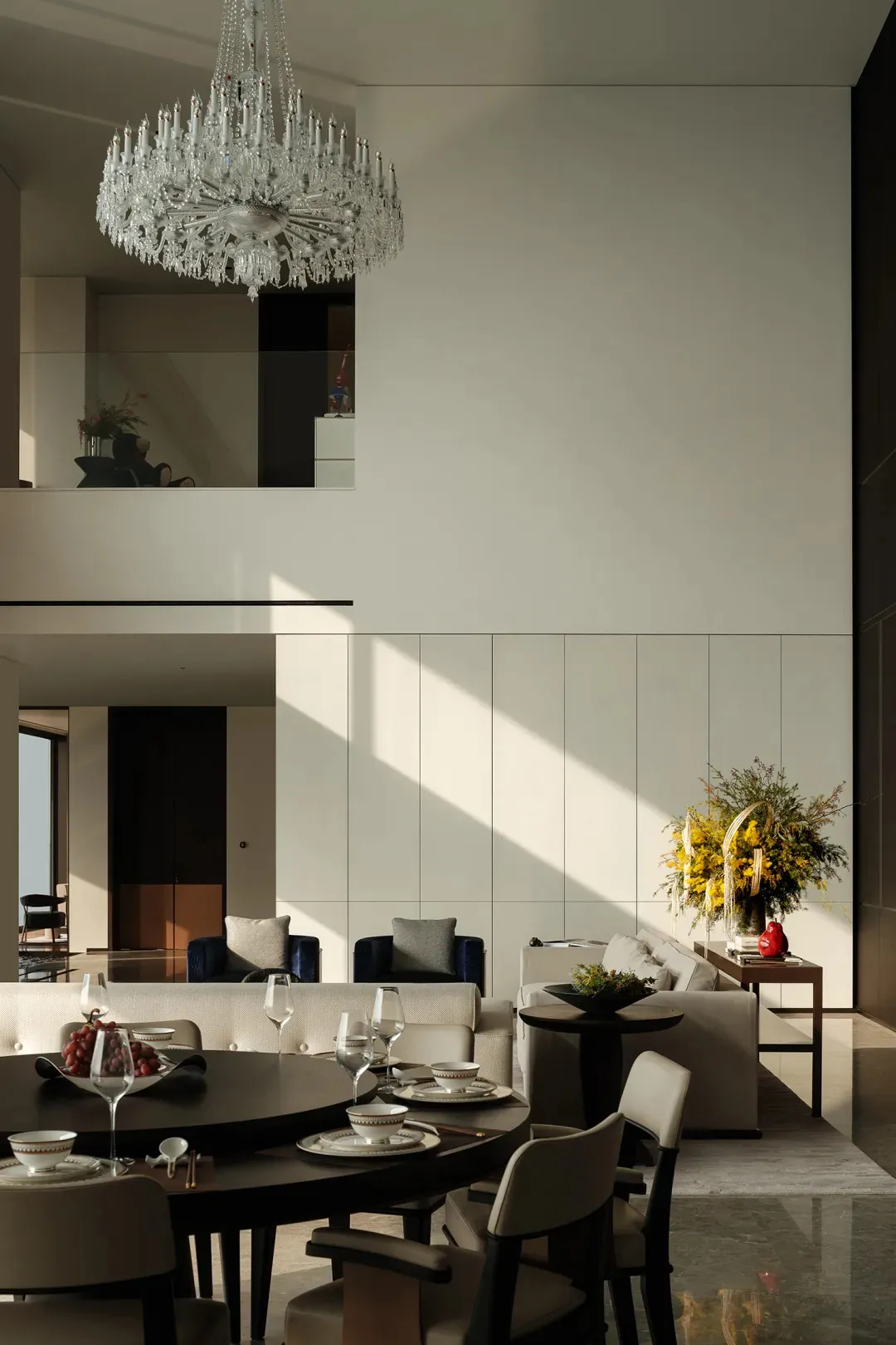 Modern living room with neutral tones, featuring a chandelier, sofas, and dining table with chairs.