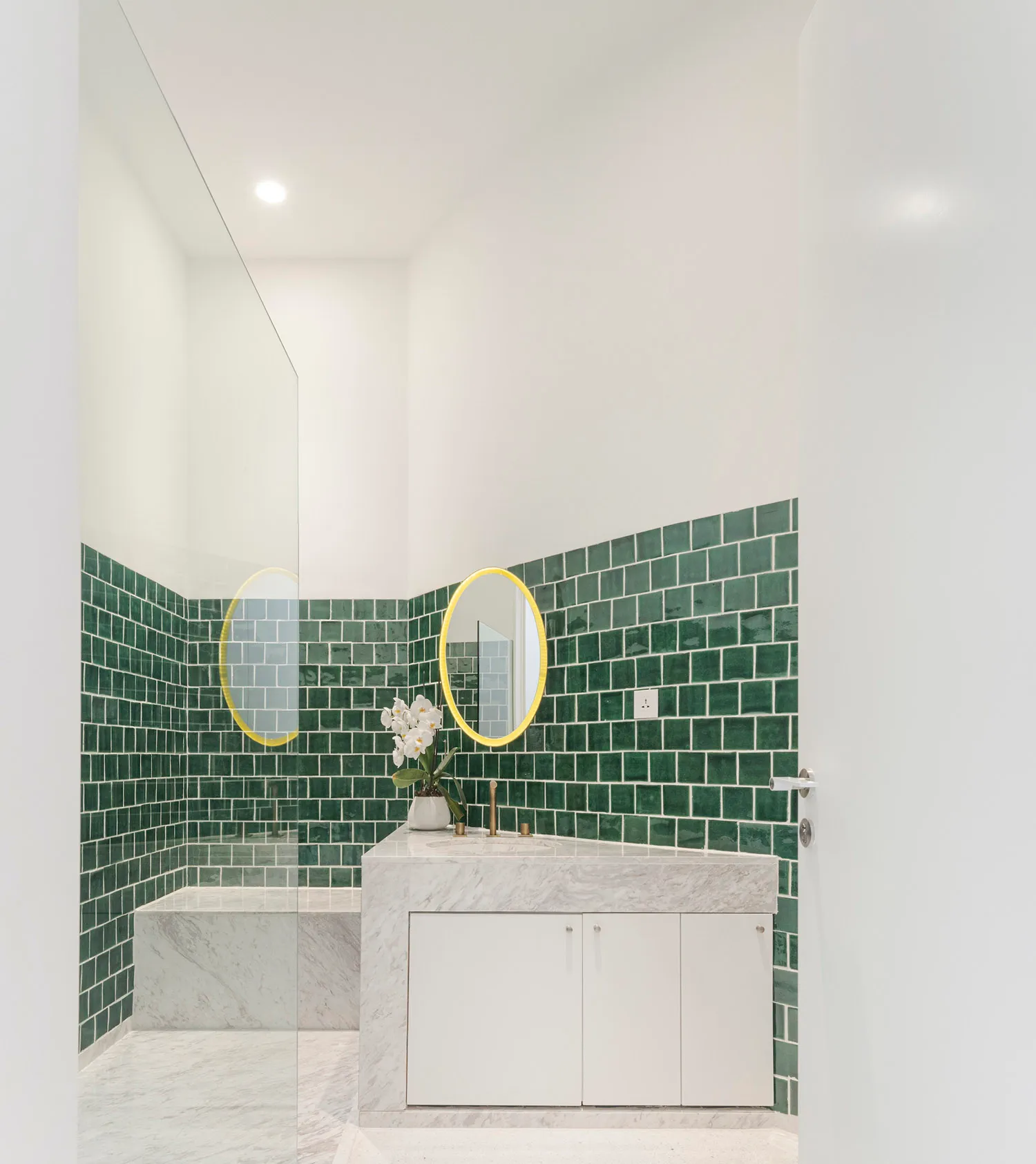 Modern minimalist bathroom featuring green tiles on the walls and a white marble counter.