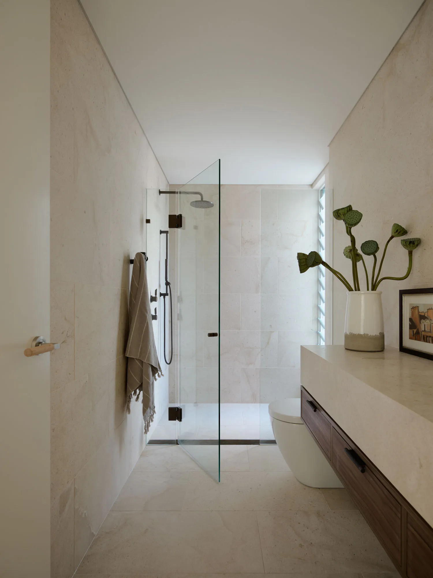 Modern minimalist bathroom with white tiled walls, floor, and ceiling, featuring a walk-in shower with glass door, a wall-mou