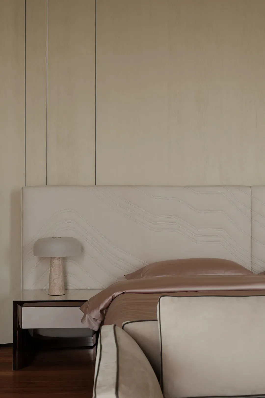 A minimalist bedroom featuring a beige upholstered bed with marble nightstand and beige fabric bedding.