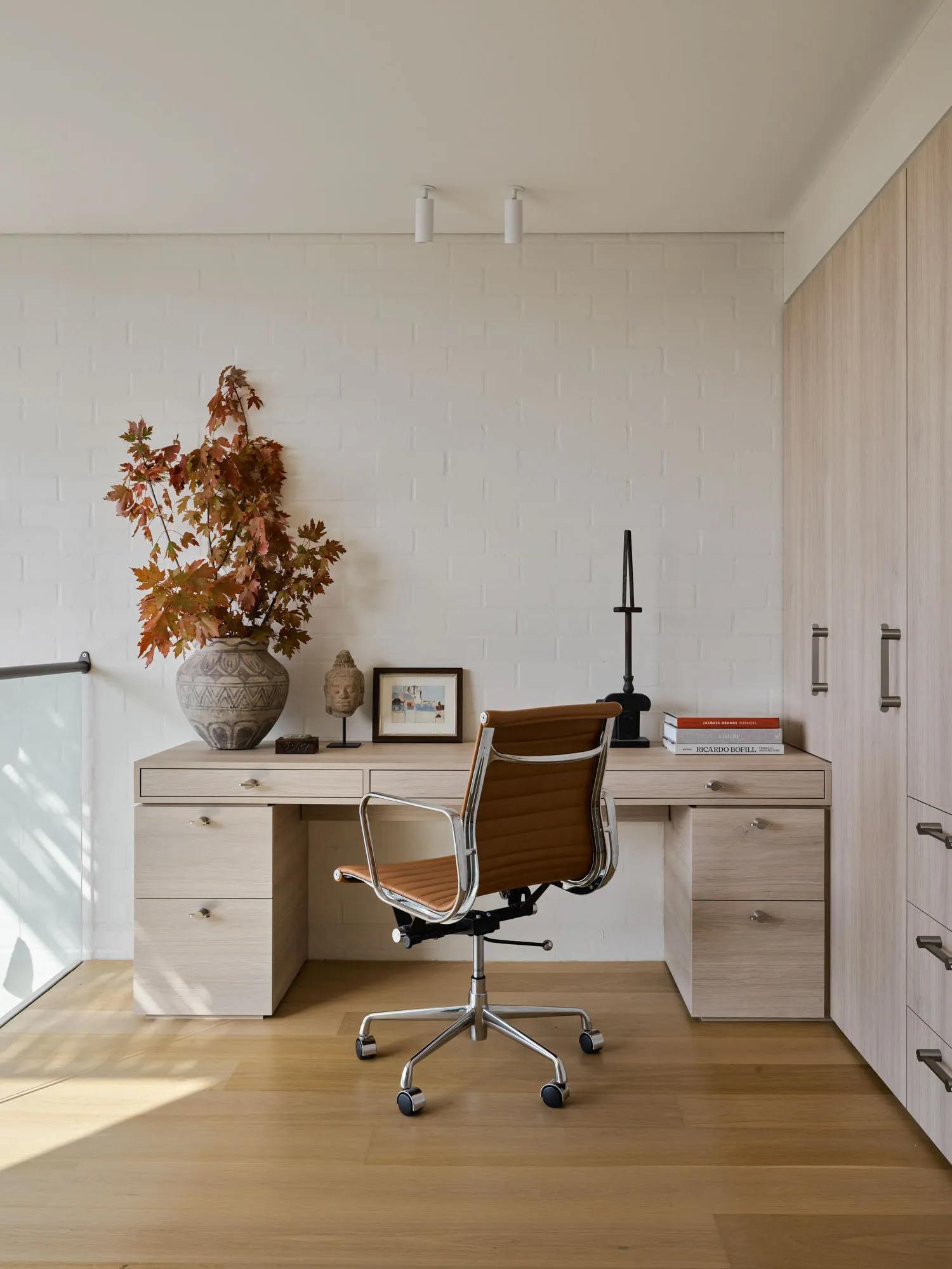 Modern workspace featuring a wooden desk and chair with a vase of autumn leaves on the desk.