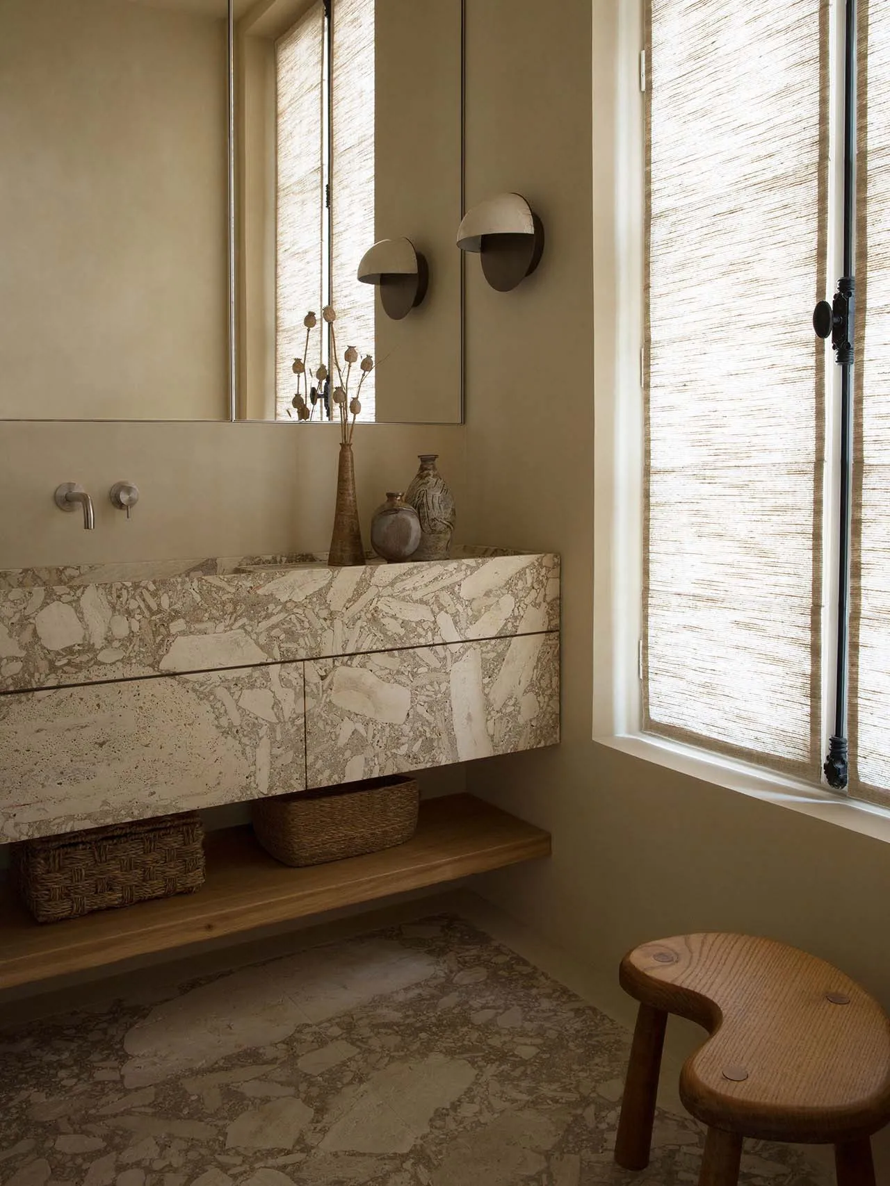 Modern, minimalist bathroom featuring a floating marble vanity, decorative vases, and woven window blinds.