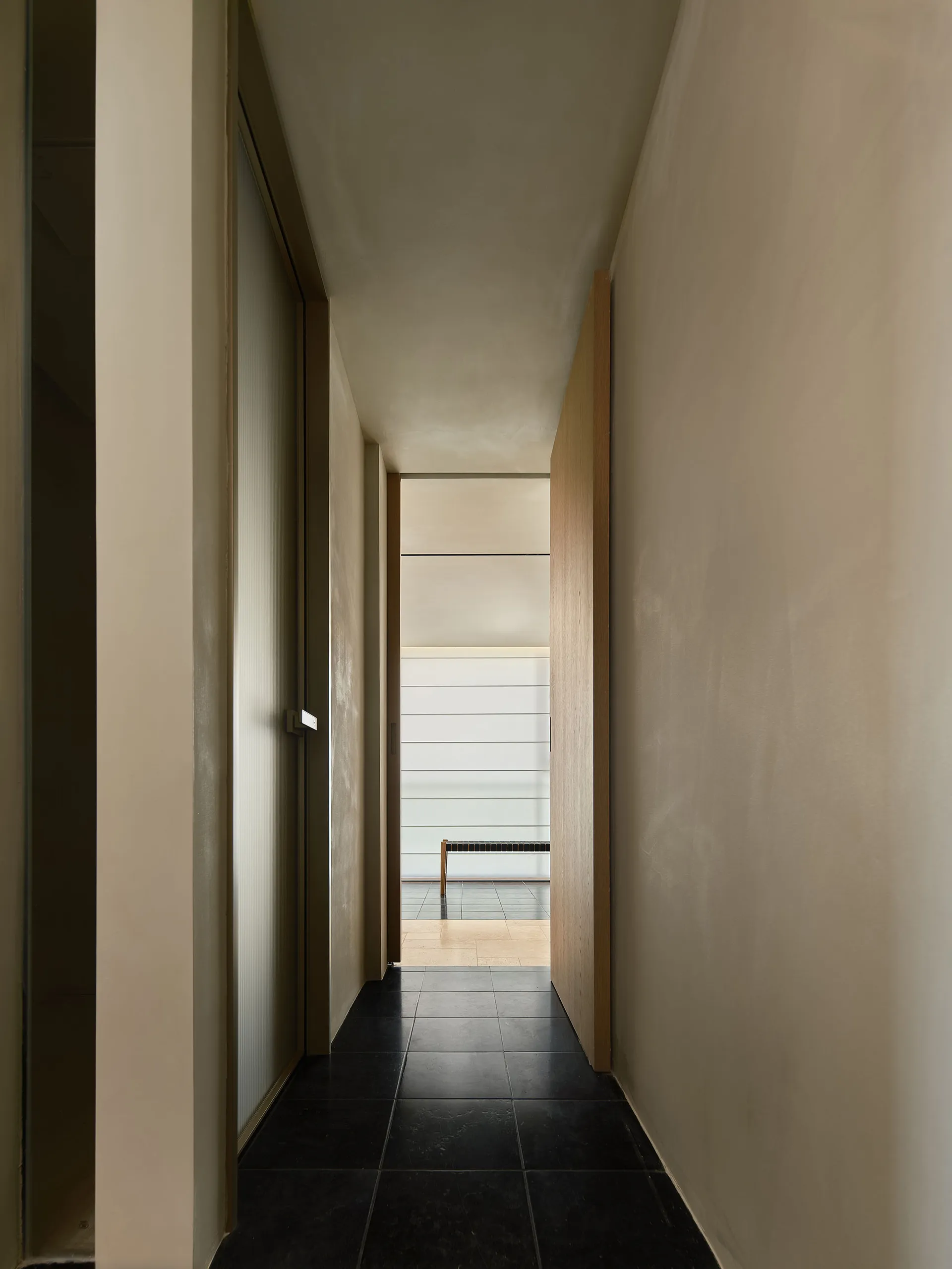 A minimalist corridor with concrete walls and floor tiles leading to a partially obscured view.