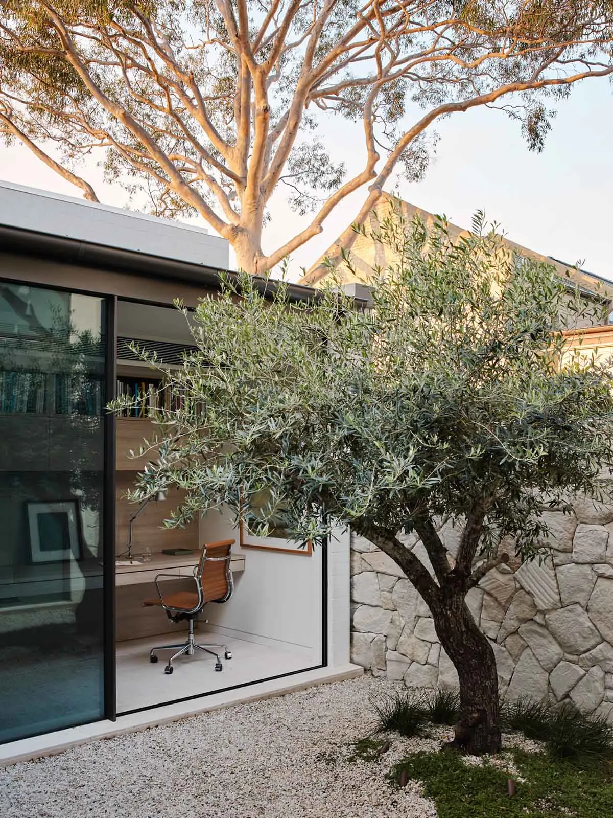 Modern minimalist home office with stone wall and wooden floor, featuring a comfortable chair and sleek desk.