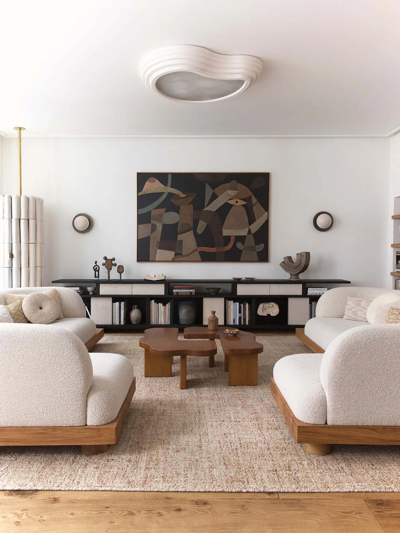 A minimalistic living room with beige wool sofas and wooden accents, featuring abstract art and a low-profile coffee table on
