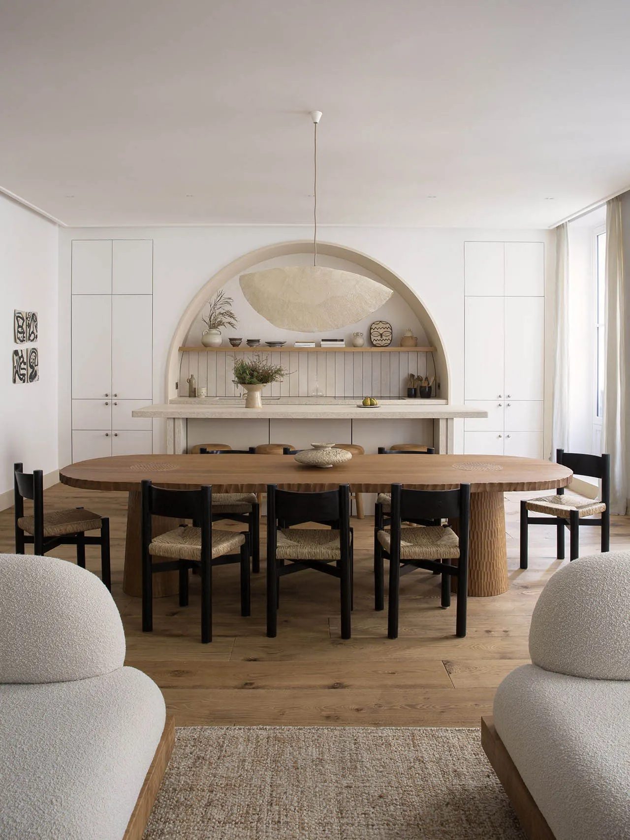 A modern, open-plan living and dining room with minimalist decor, wooden furnishings, and a marble counter.