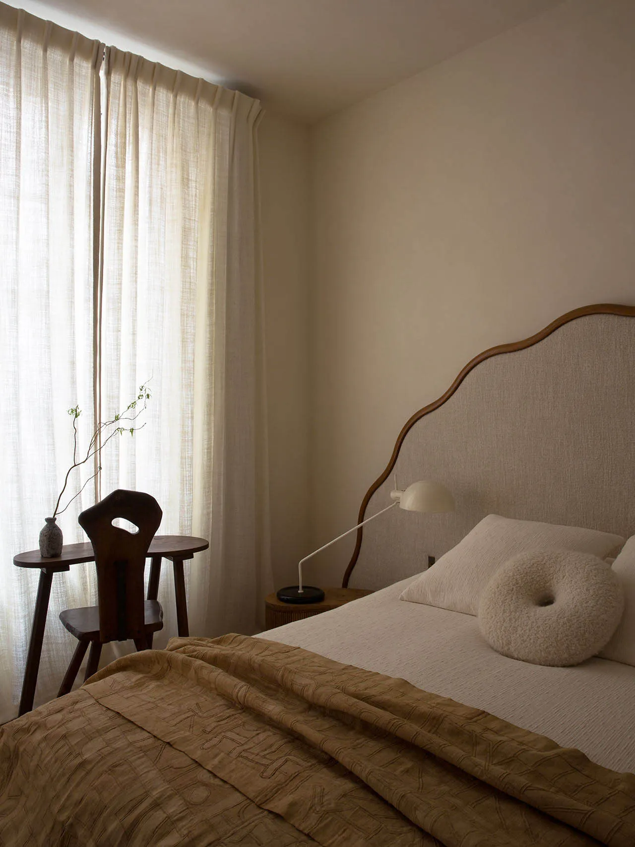A modern minimalist bedroom featuring soft textiles, wooden furniture, and linen curtains.