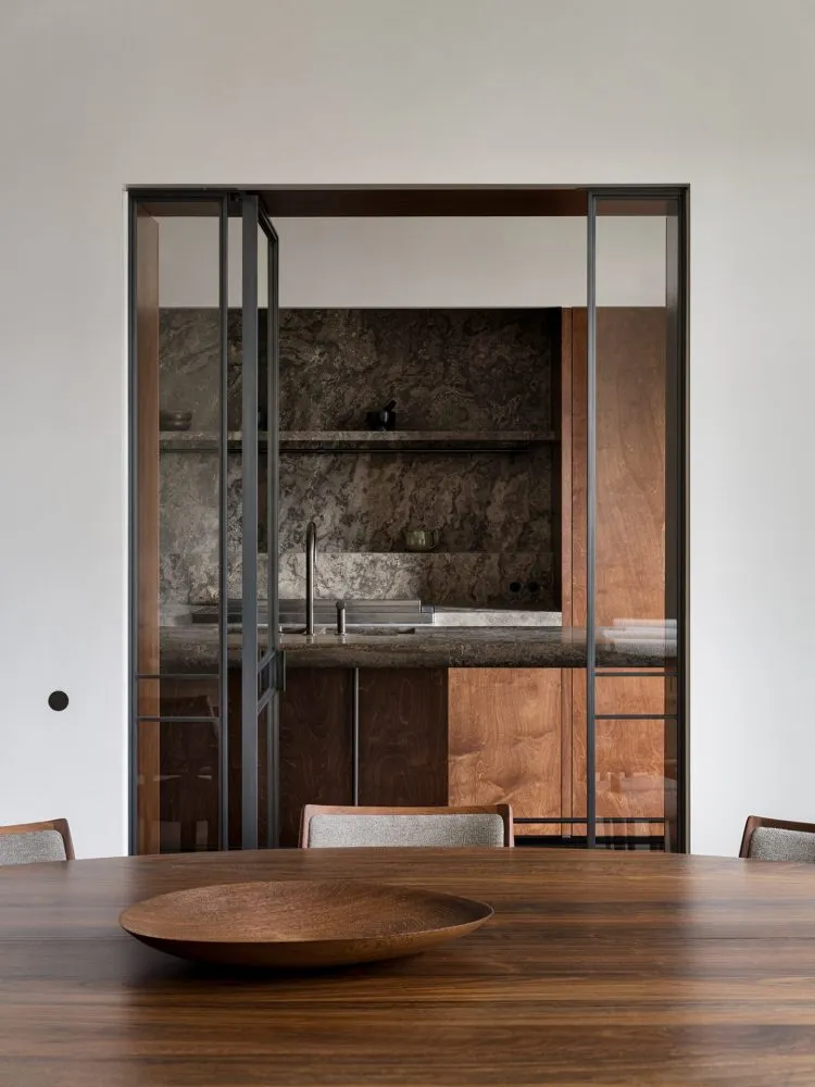 Modern, minimalist kitchen with a wooden table and marble countertops.
