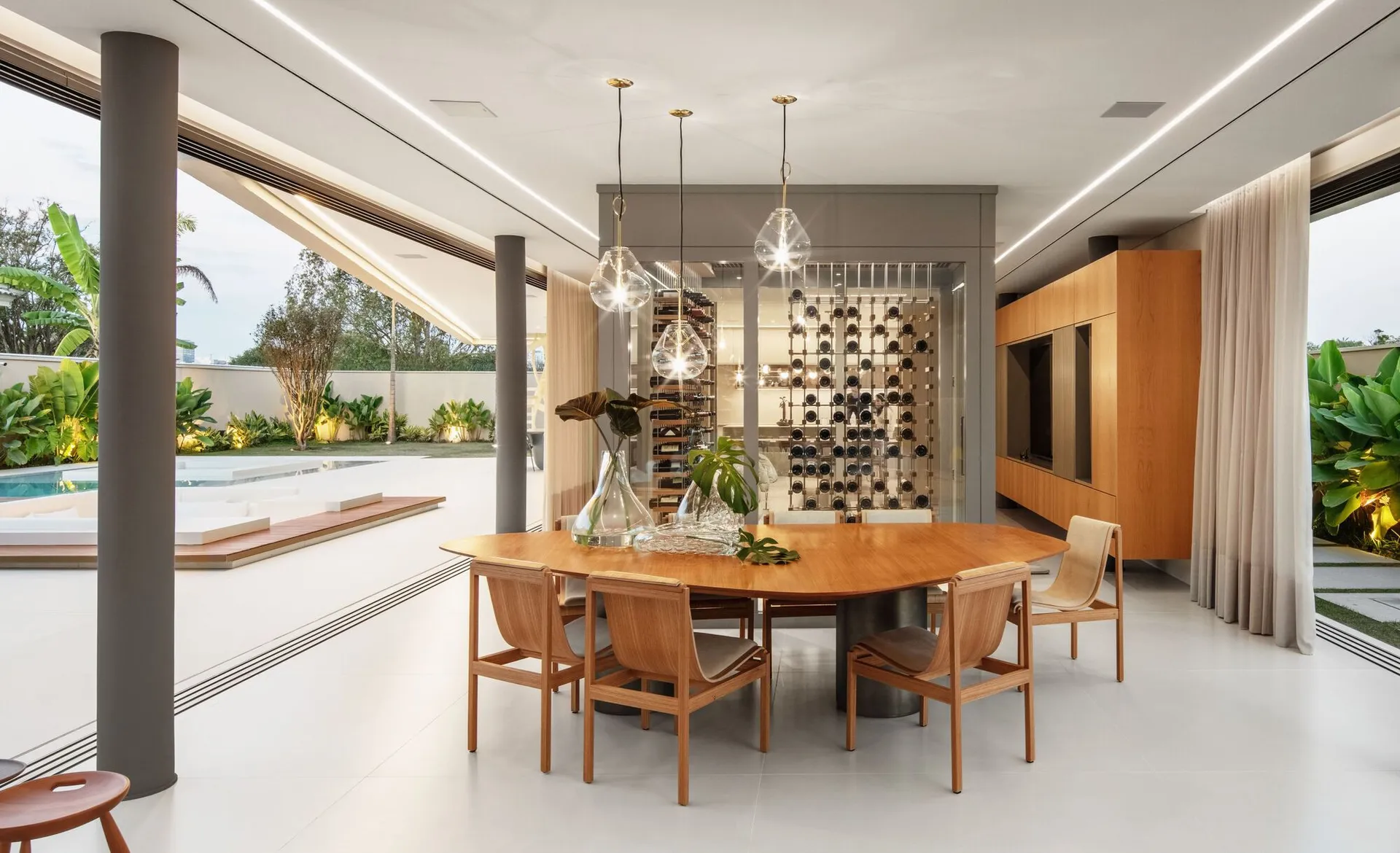 Modern minimalist residential kitchen with a wooden dining table and chairs, glass pendant lights, and a view of the outdoor