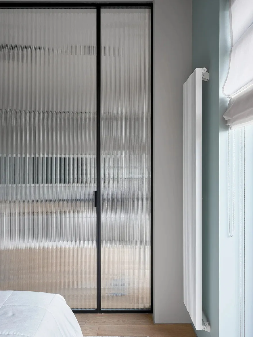 Minimalist bedroom featuring frosted glass panels and white radiator.