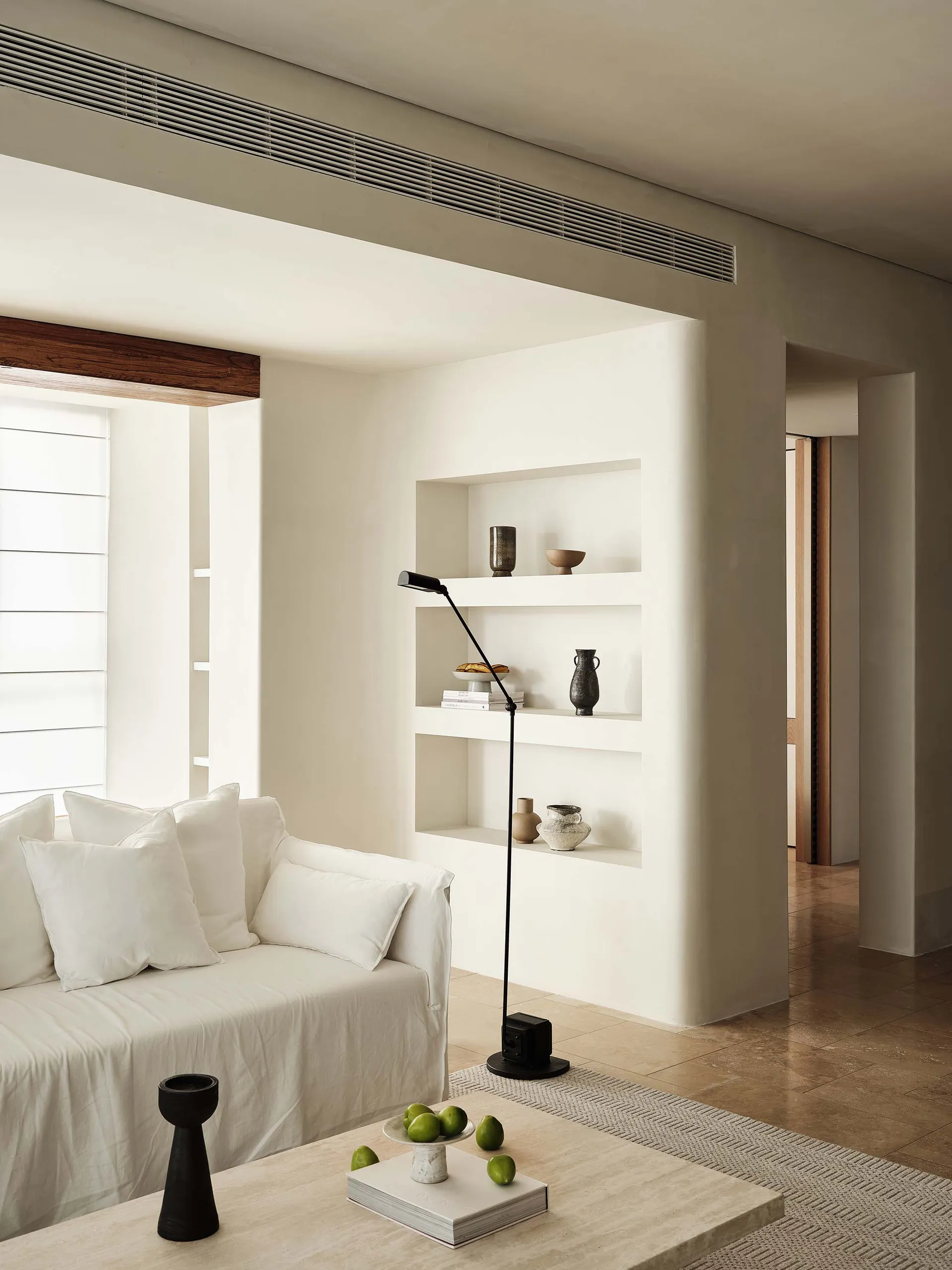 A minimalist living room featuring neutral-toned walls, a white sofa, and a coffee table with green apples.