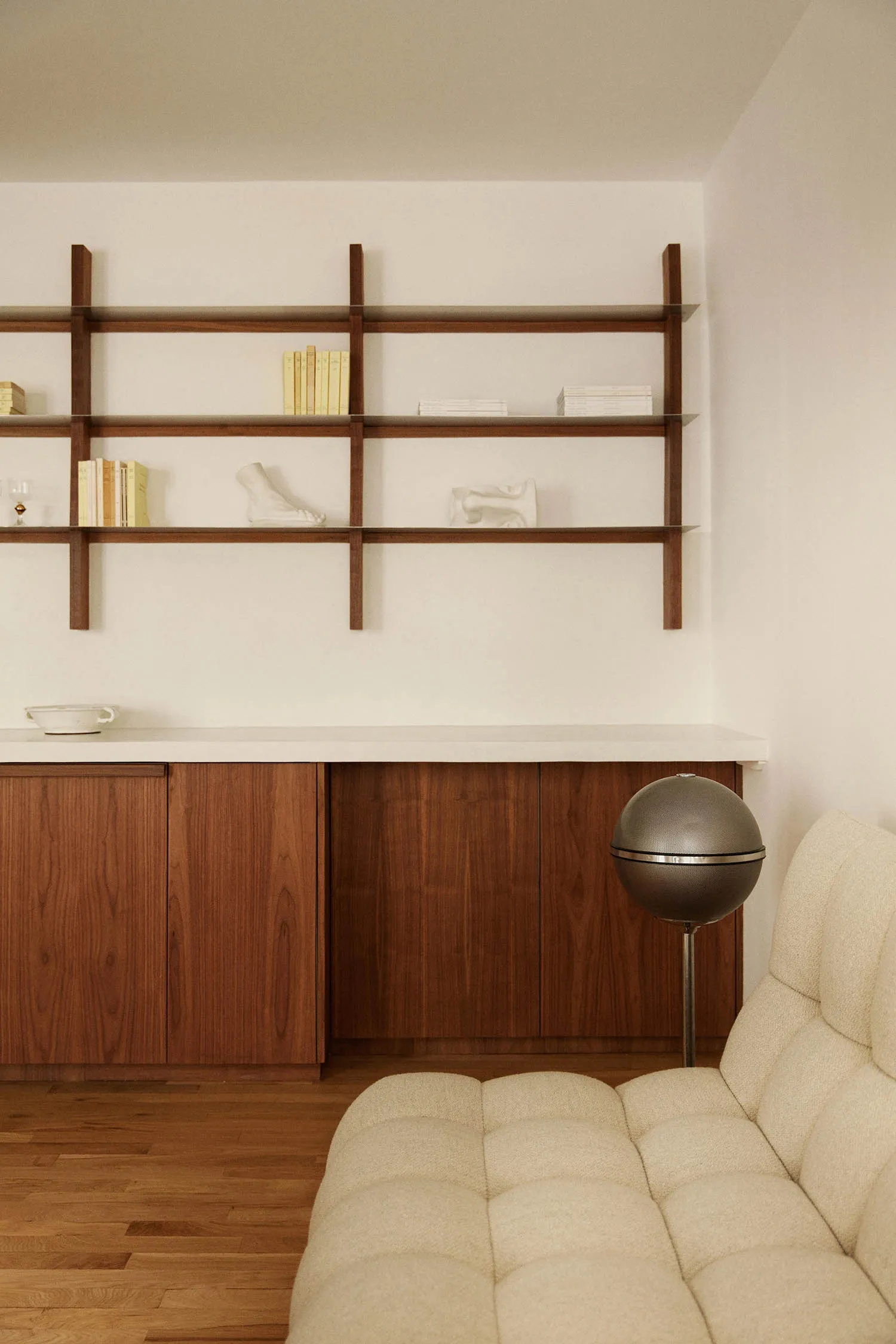 A modern minimalist living room featuring a wooden cabinet, white sofa, and sleek shelving unit.