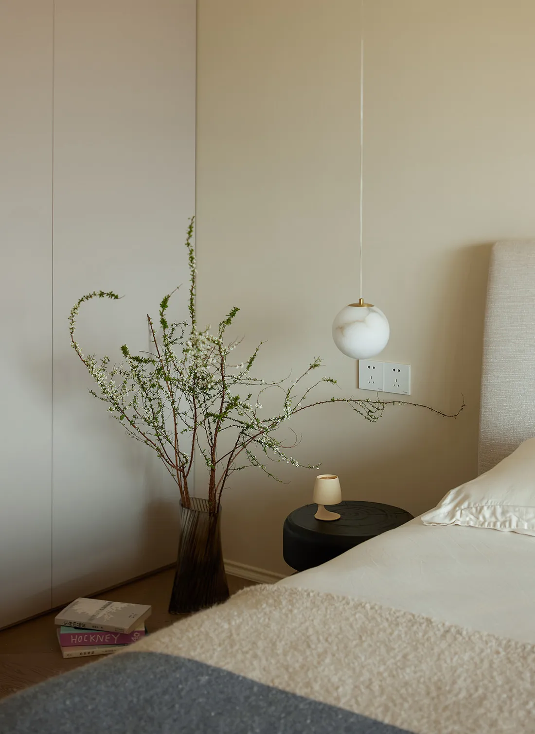 A modern bedroom featuring a bed with a beige cover and a black circular side table with a small white cup on it.