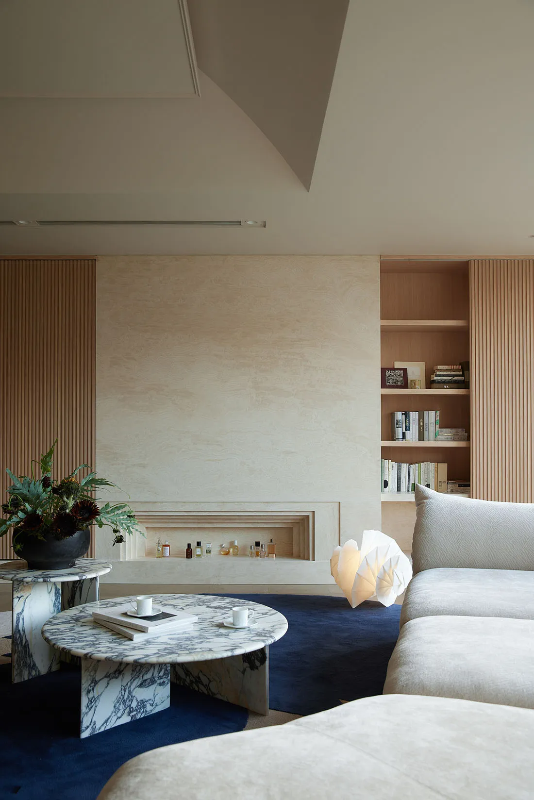 A modern living room featuring a marble coffee table, wooden shelves, and a white sofa on a blue rug.