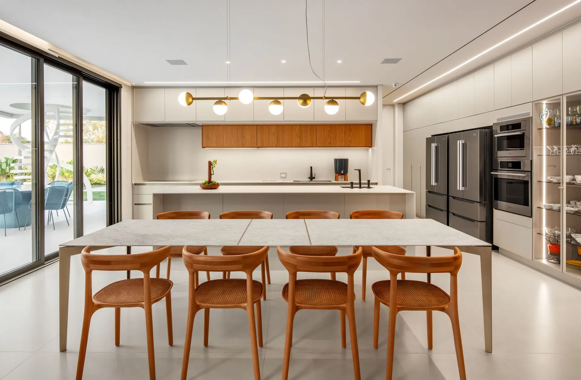 A modern residential kitchen featuring a large marble island counter and an adjacent dining table with wooden chairs.