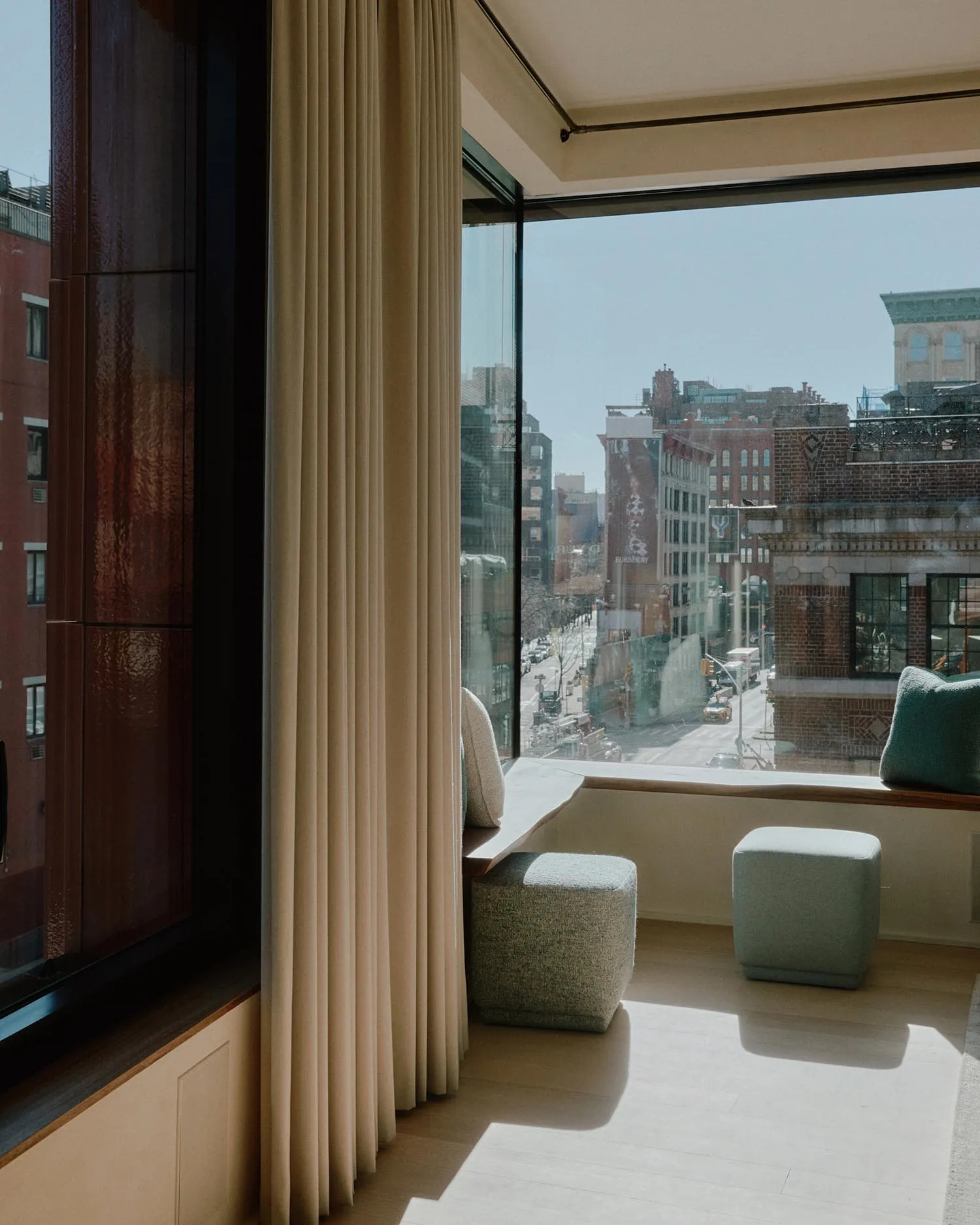 A modern interior space featuring a window sill with fabric seating and cushions, overlooking a cityscape through a large win