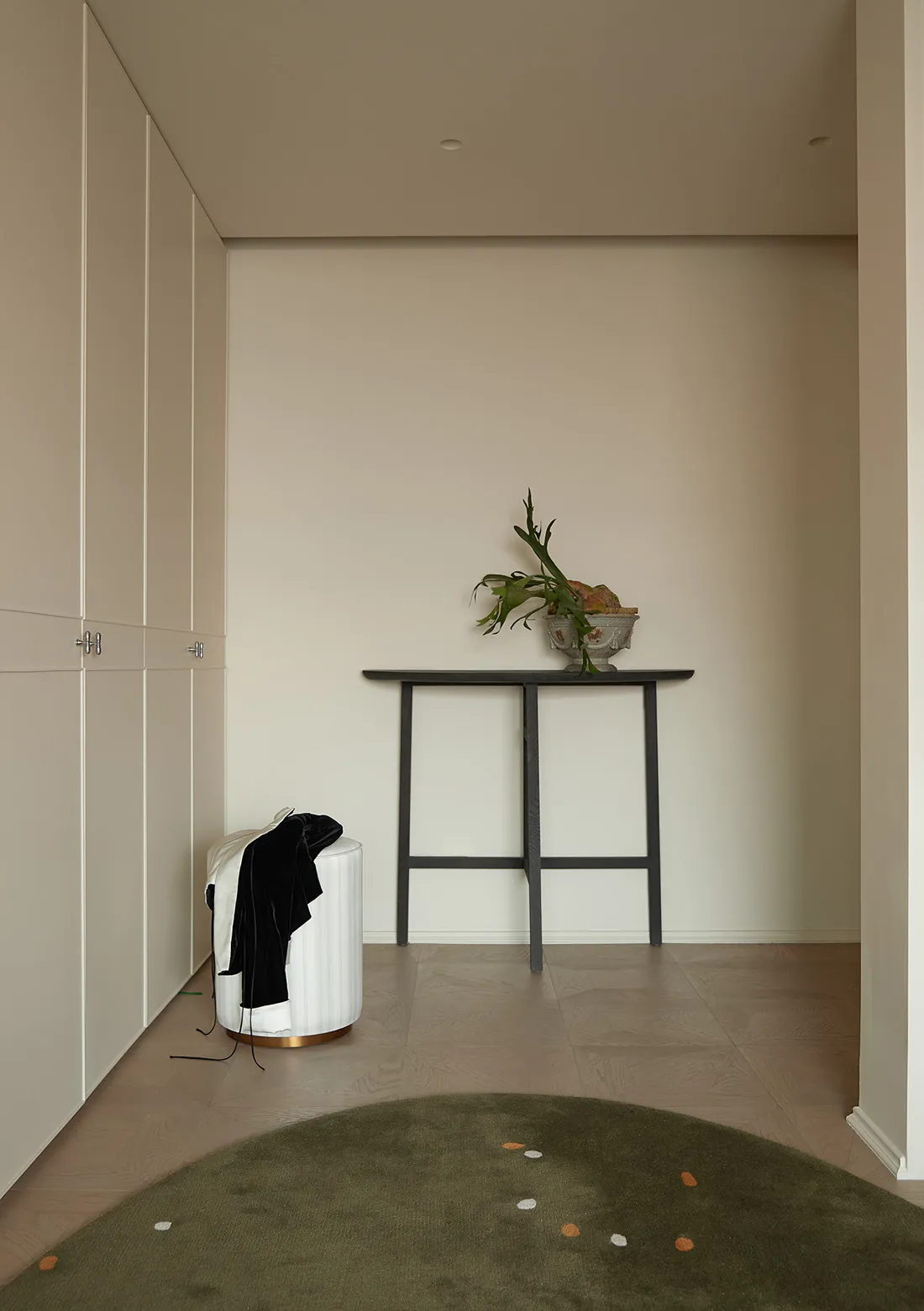 A minimalist entryway with neutral-toned walls, a wooden table, and a green rug with small white dots.