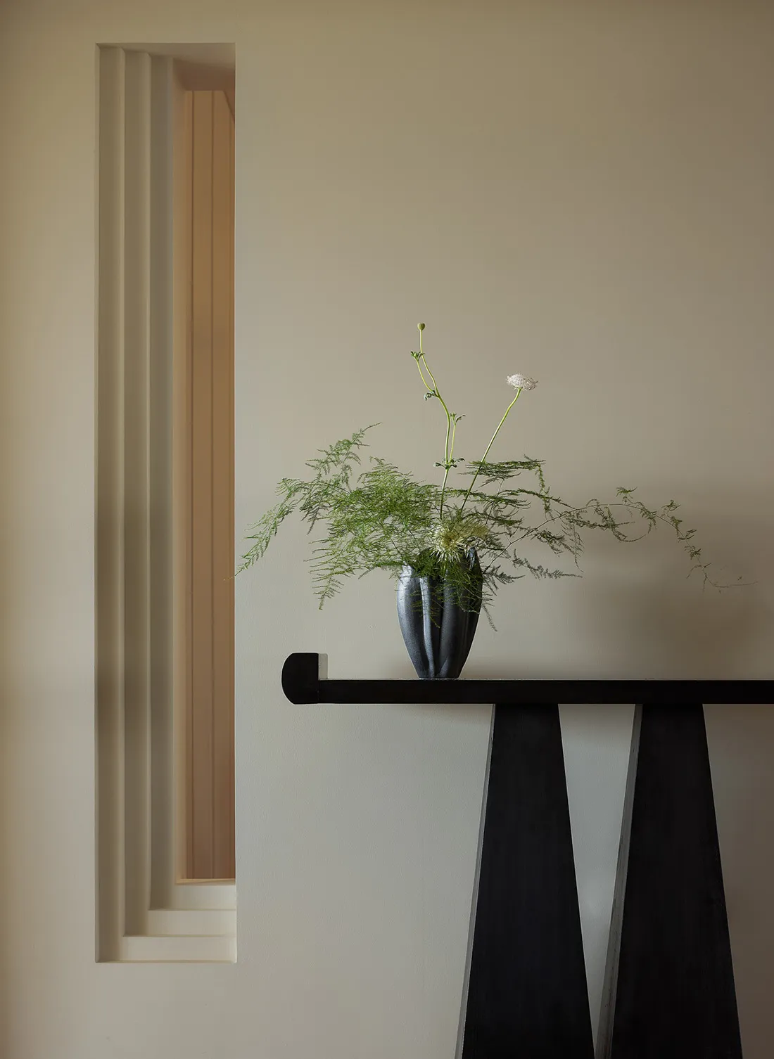 A minimalist decorative plant arrangement featuring a ceramic vase with green foliage and a small white flower, placed on a s