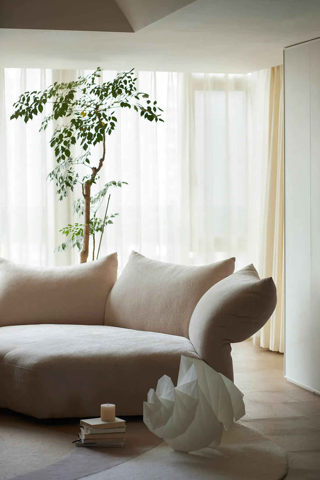 A minimalist living room featuring a boucle sofa, a potted plant, and a decorative paper swan on a rug.