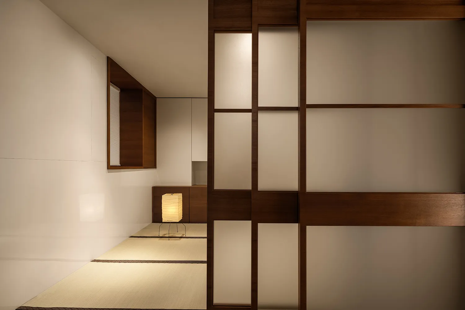 A minimalist residential interior featuring a paper lamp, tatami mat, and wood and fabric materials.