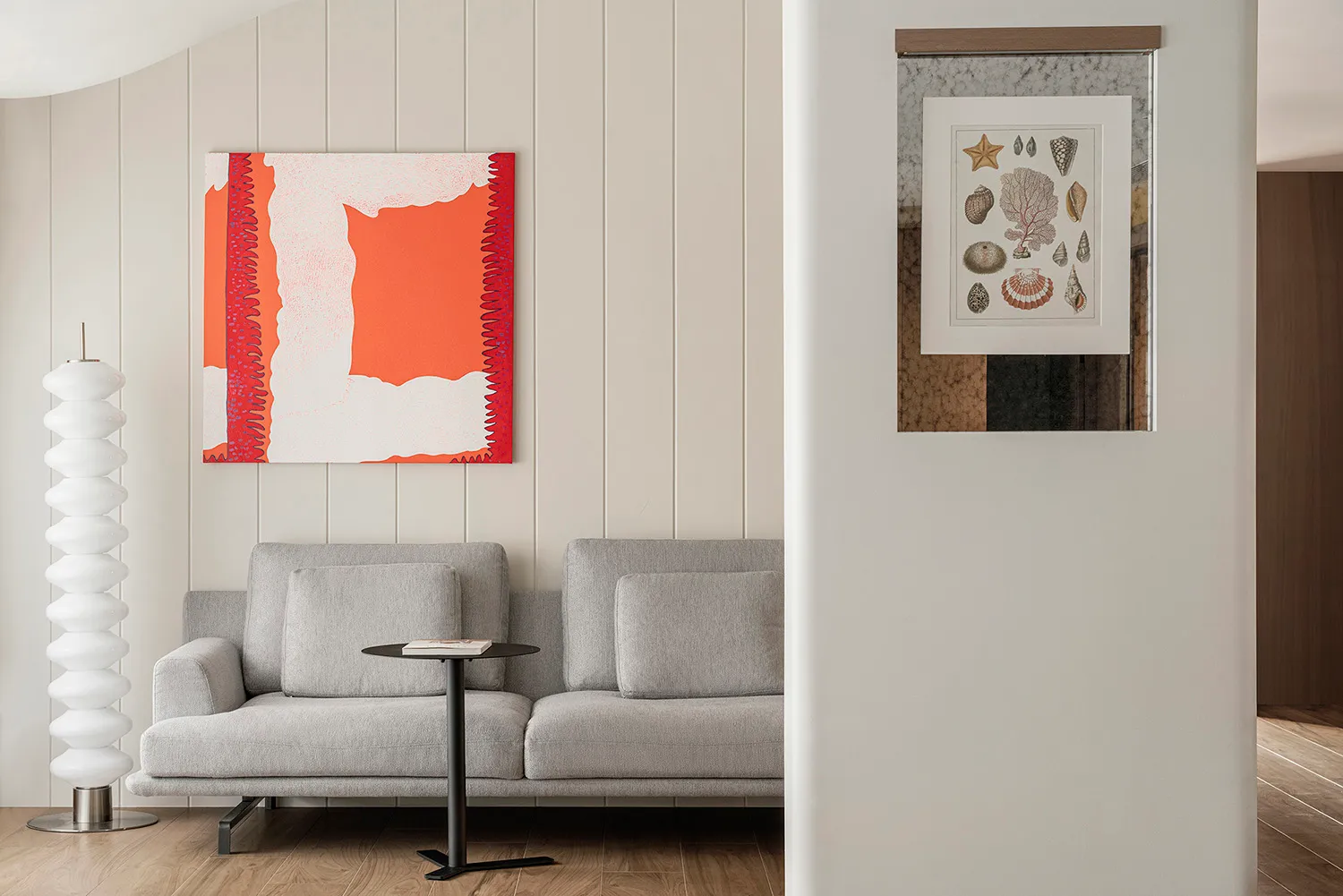 Light gray fabric couch sitting against a white paneled wall with an abstract art piece featuring vibrant red and white color