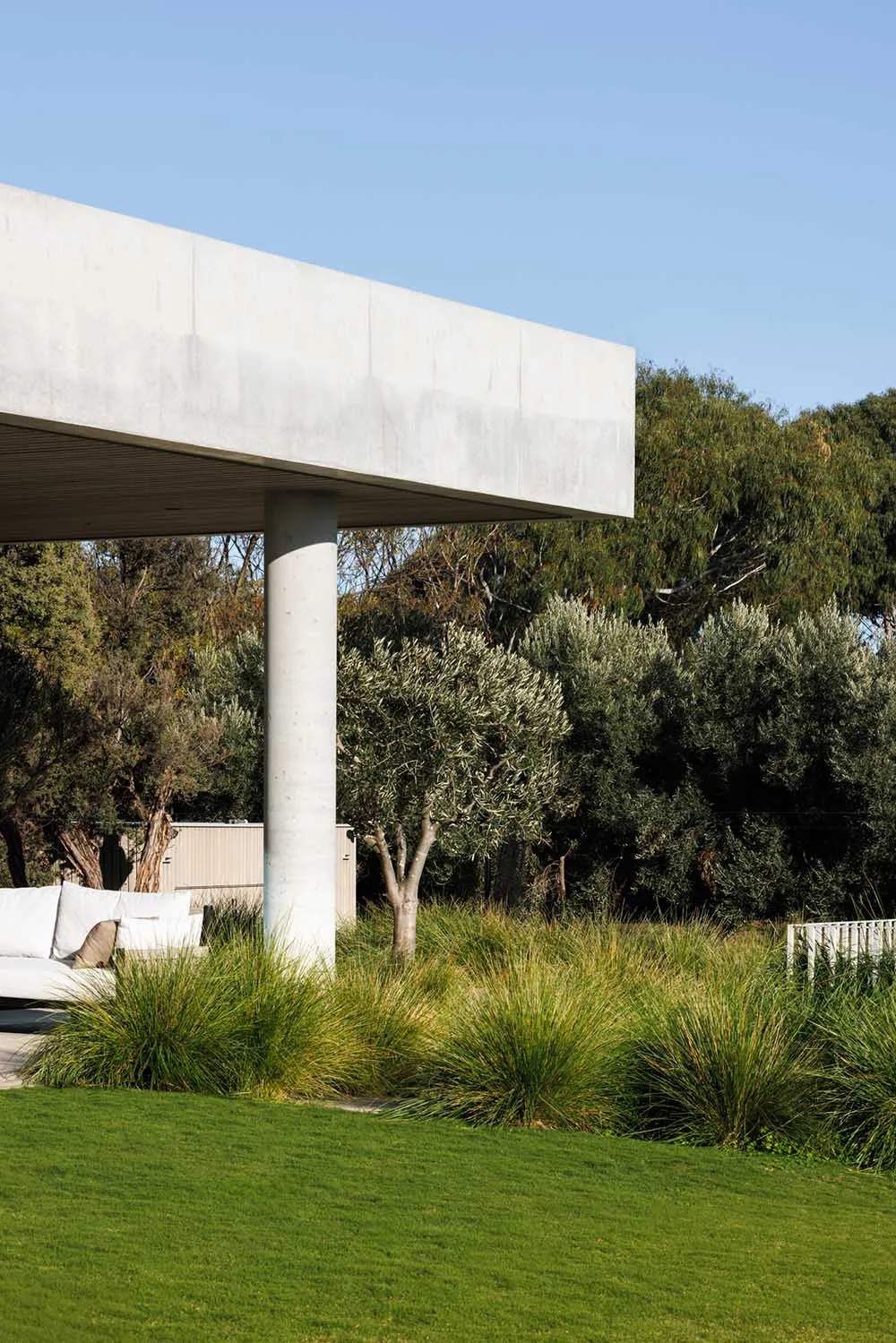 Minimalist architectural design with concrete structure, green grass, and planted trees outdoors.