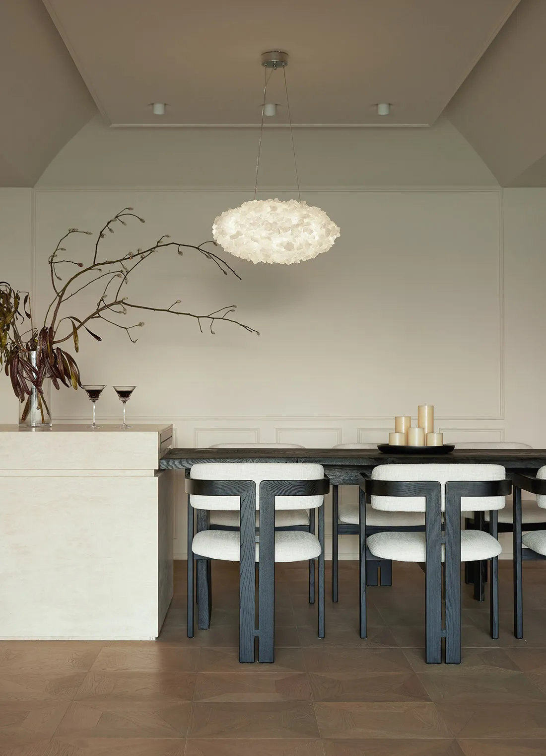 Modern minimalist dining room with wooden table and white upholstered chairs, featuring a unique cloud-shaped pendant light a
