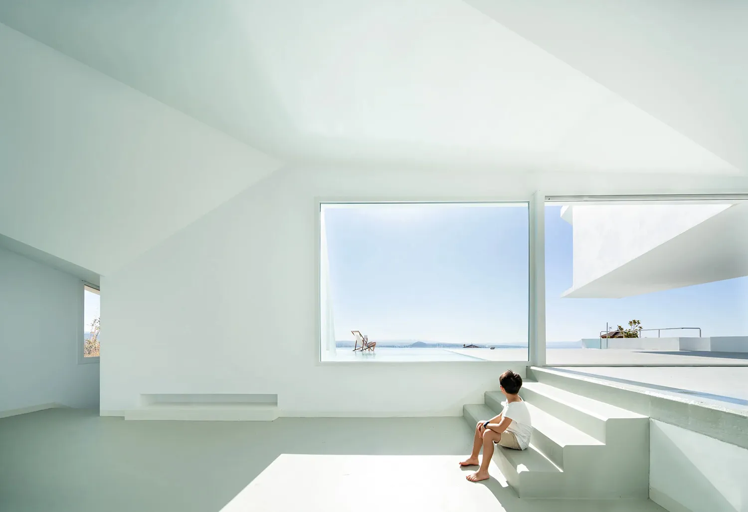 A minimalist interior space featuring concrete flooring and walls, with a large sliding glass window showcasing an outdoor po