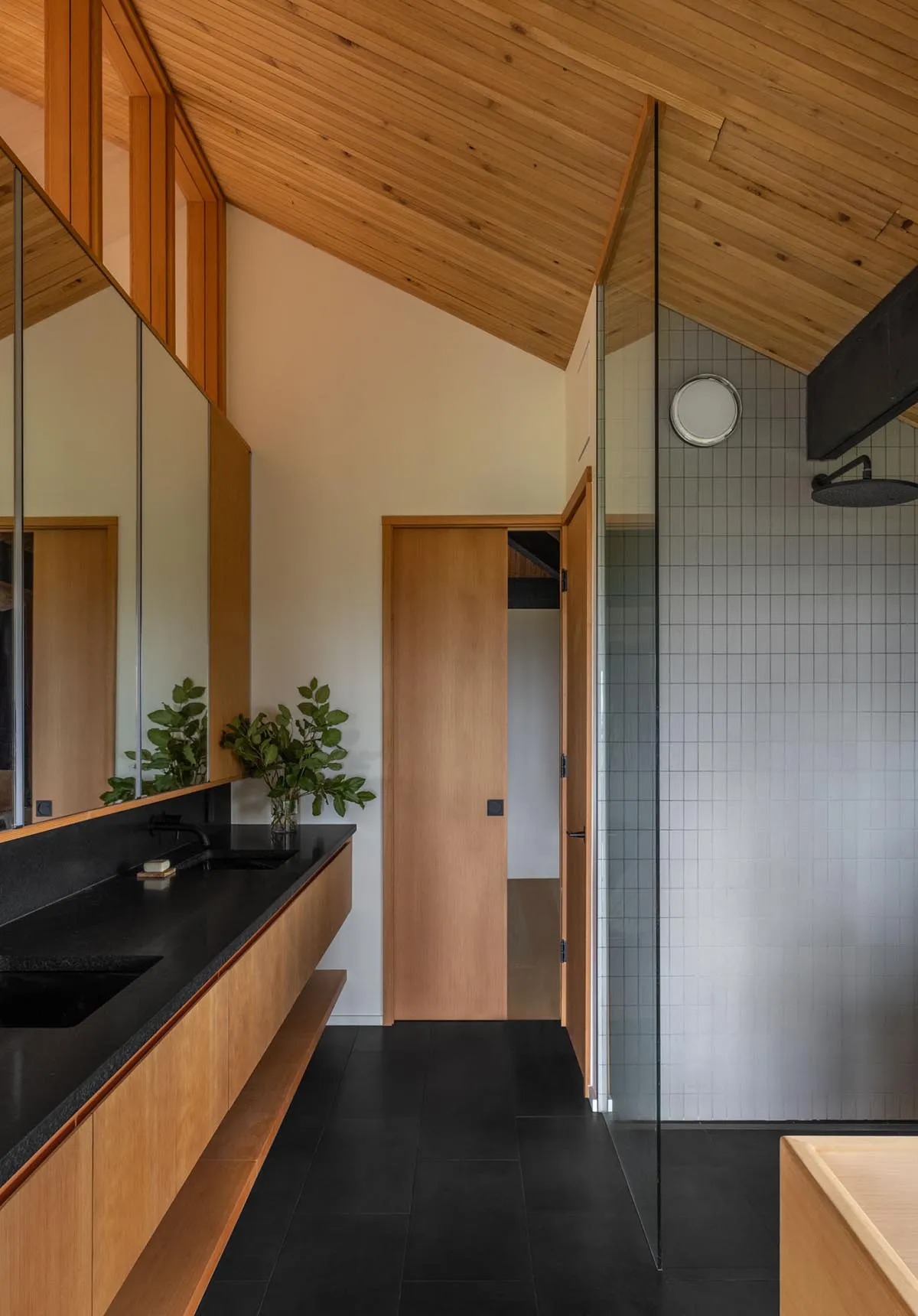 A modern bathroom with wooden cabinets, glass shower enclosure, and stone countertops.