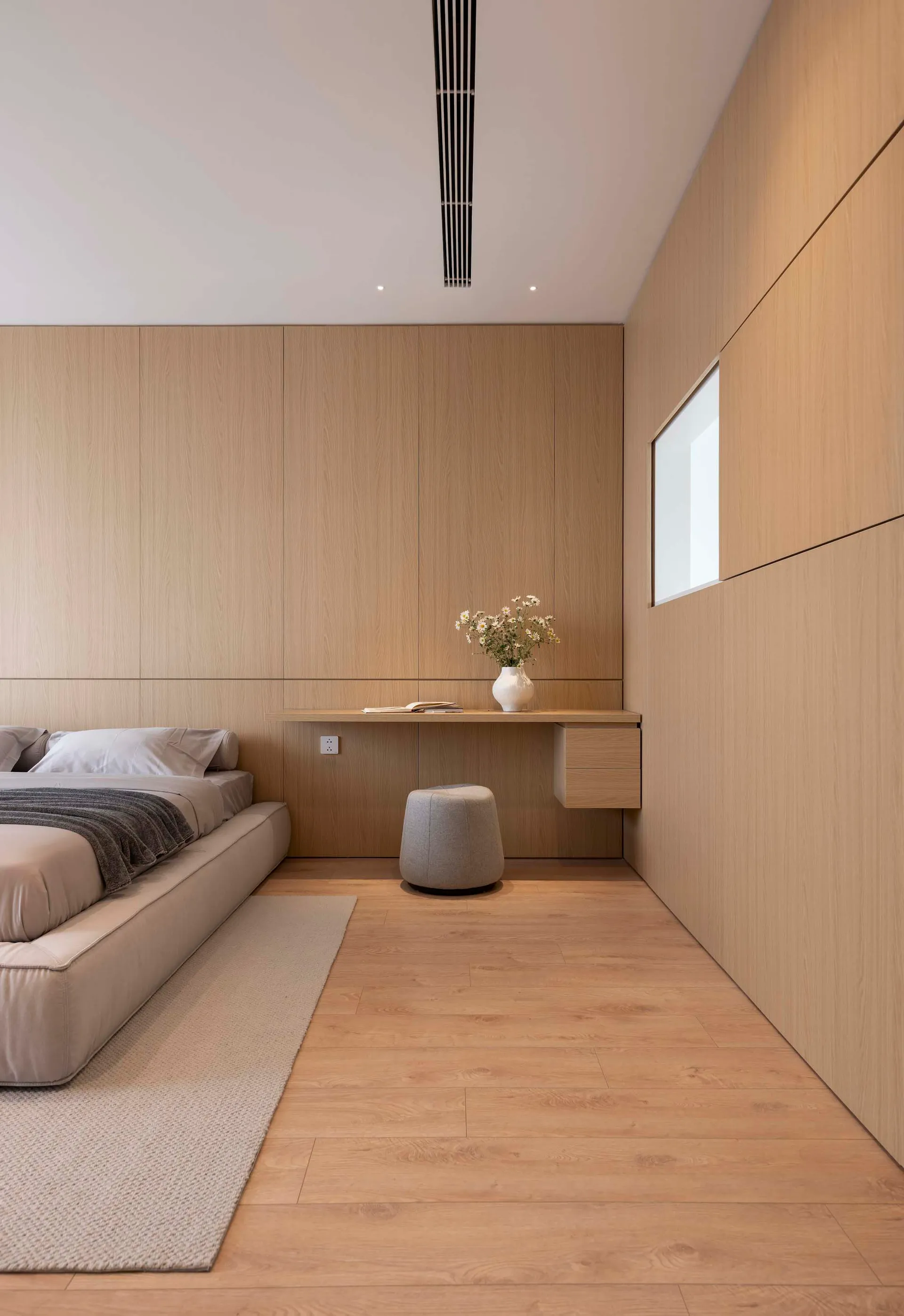 Modern bedroom with wooden furniture, featuring a minimalist design and a small desk with a vase of flowers.
