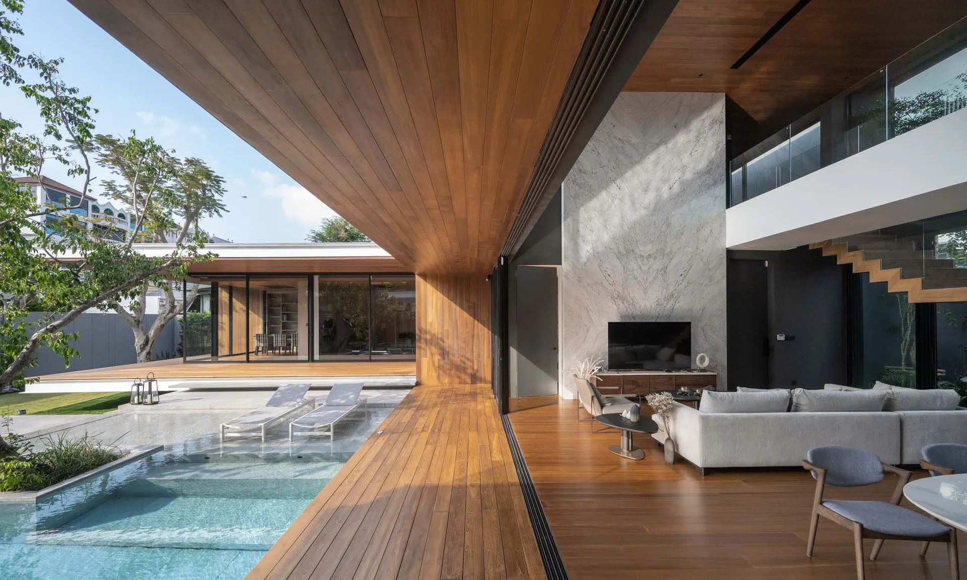 A spacious, modern residential living room with wooden flooring and a large outdoor area with a pool and lounge chairs.