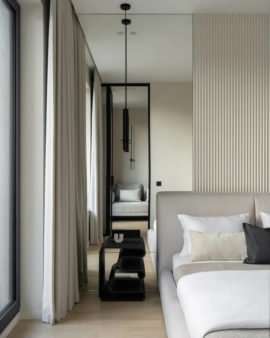 Modern minimalist bedroom featuring a light-colored upholstered bed with white and cream-colored pillows and a black circular