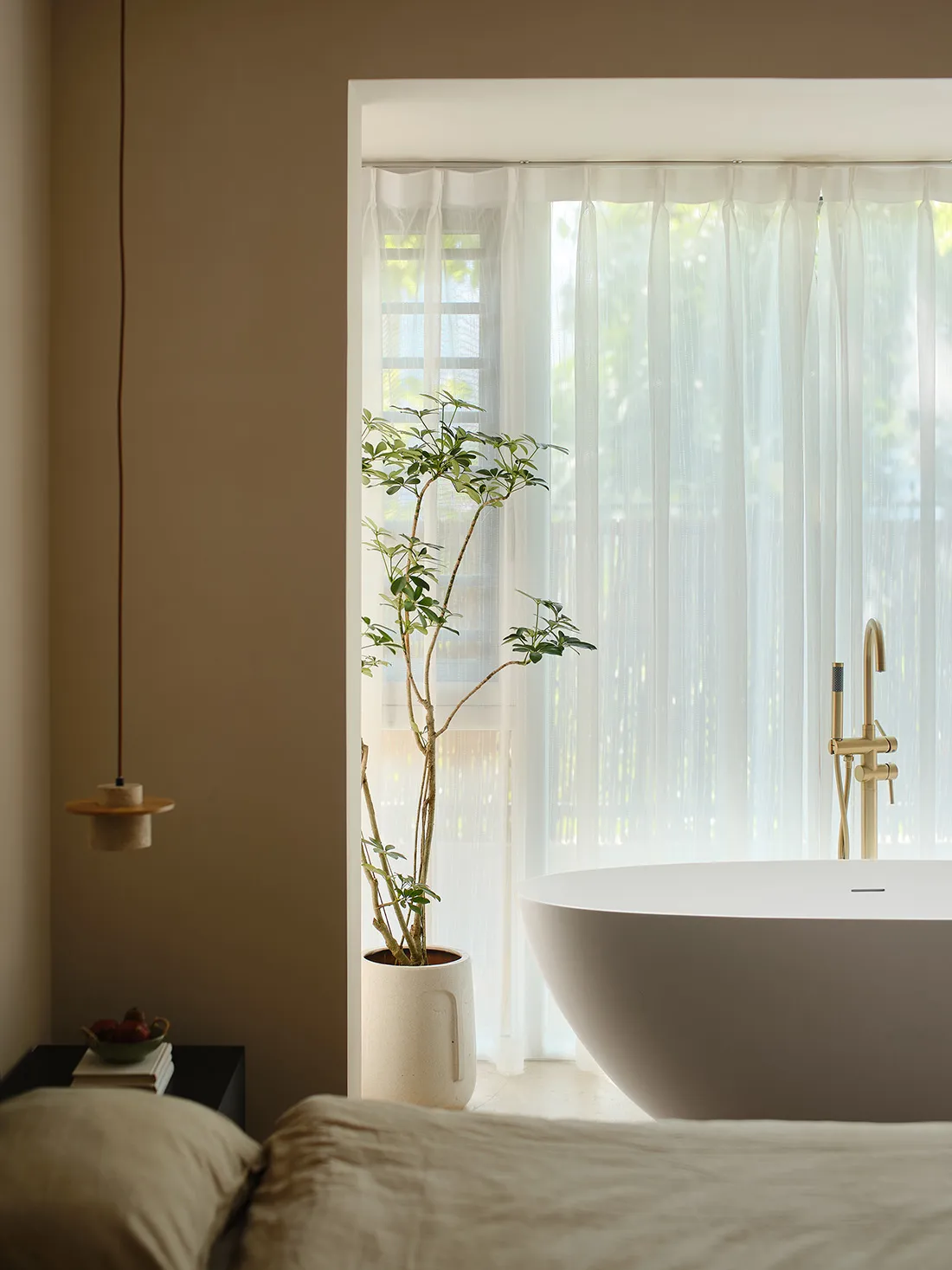 A minimalist bedroom featuring a white bathtub, sheer white curtains, and light-colored fabric bedding.