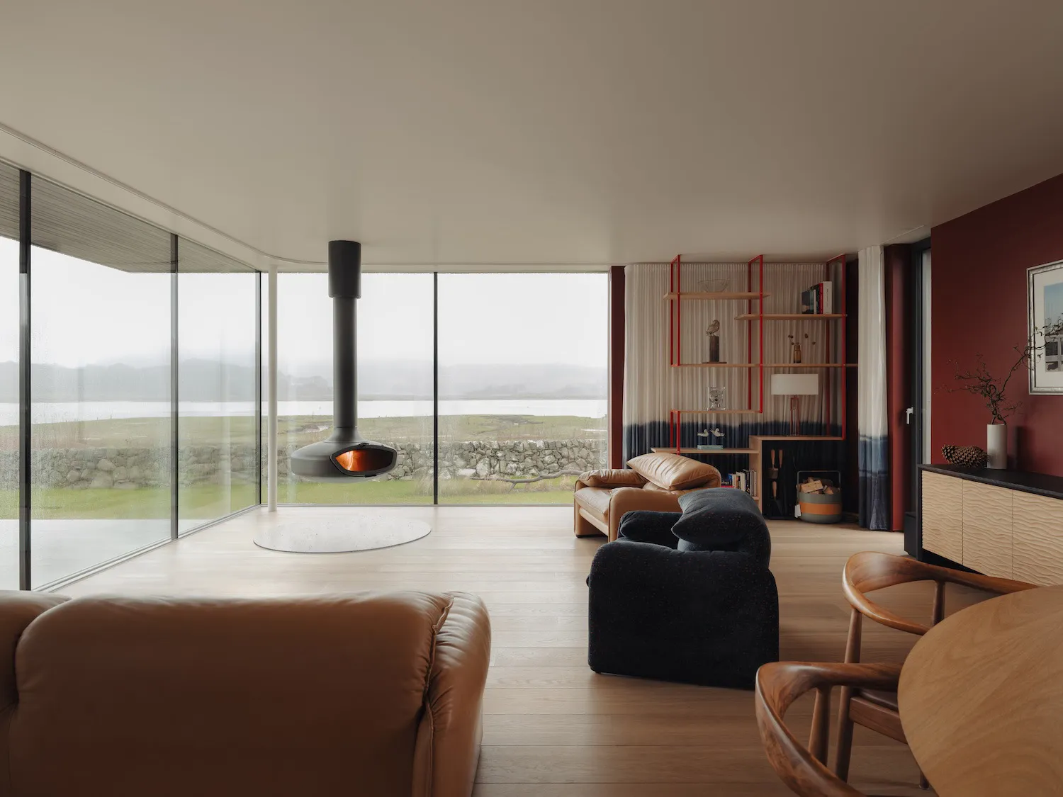 Modern living room featuring timber flooring, furniture, and windows overlooking a scenic landscape.