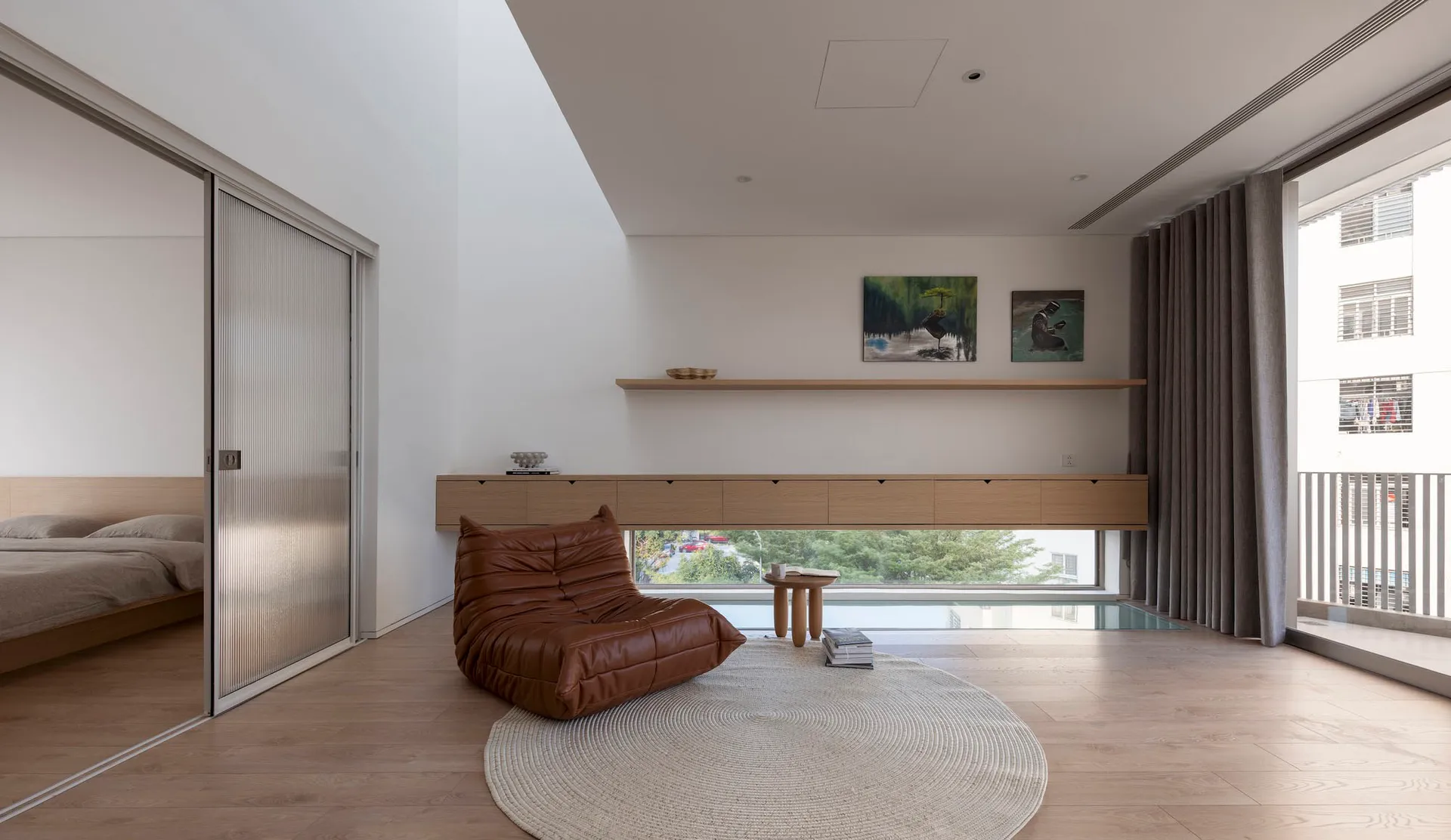 A minimalist living room featuring a brown leather sofa, wooden flooring, and a circular rug.