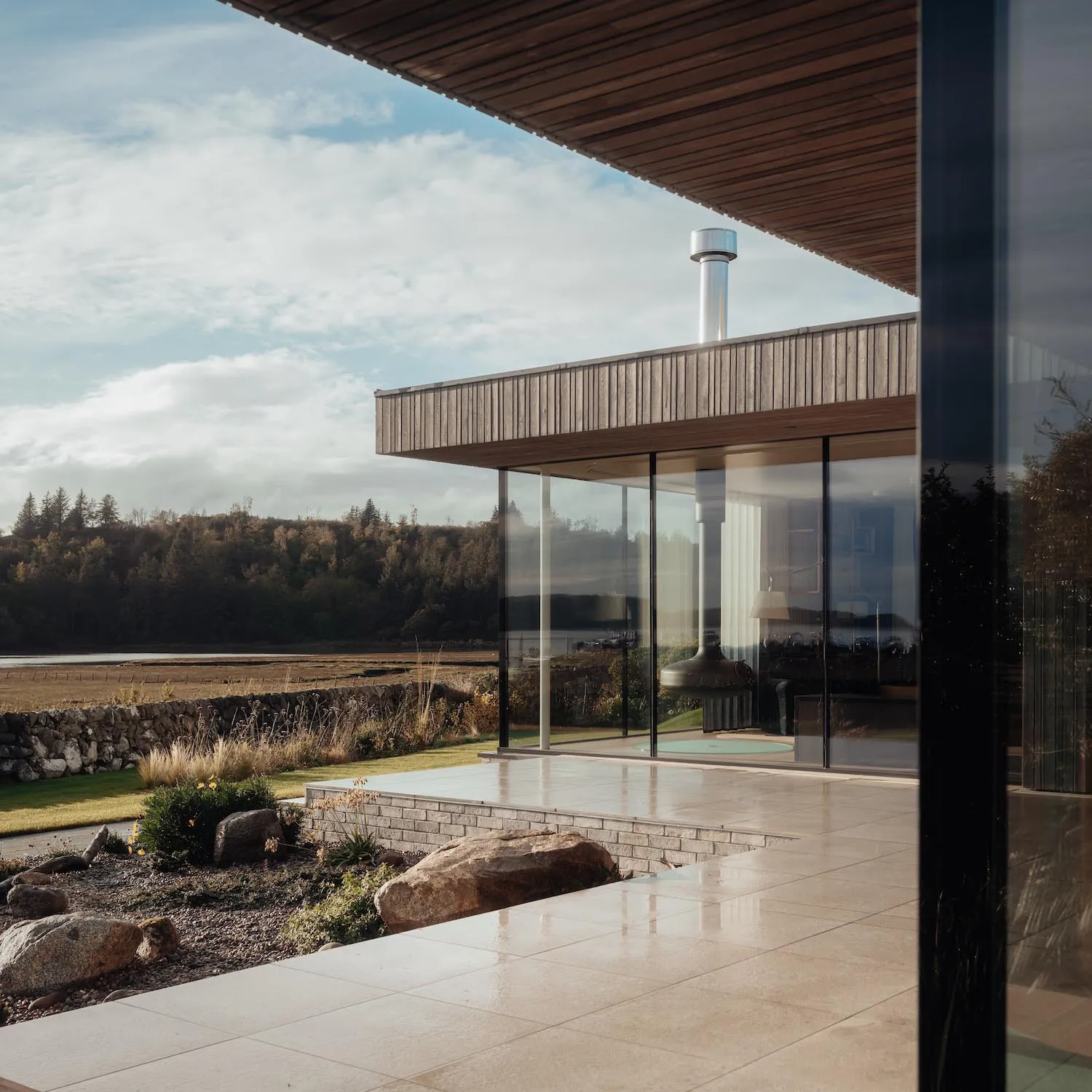 A modern residential exterior featuring glass windows, stone accents, and natural wood elements.