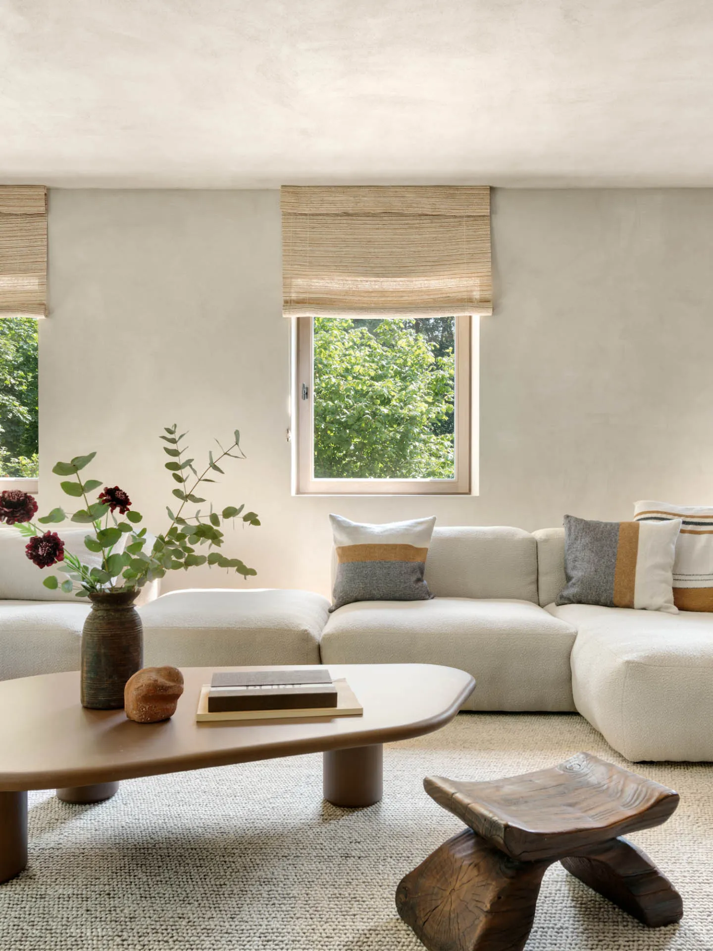 A modern, neutral-toned living room featuring a modular sofa, a wooden coffee table with decorative items, and a natural wood
