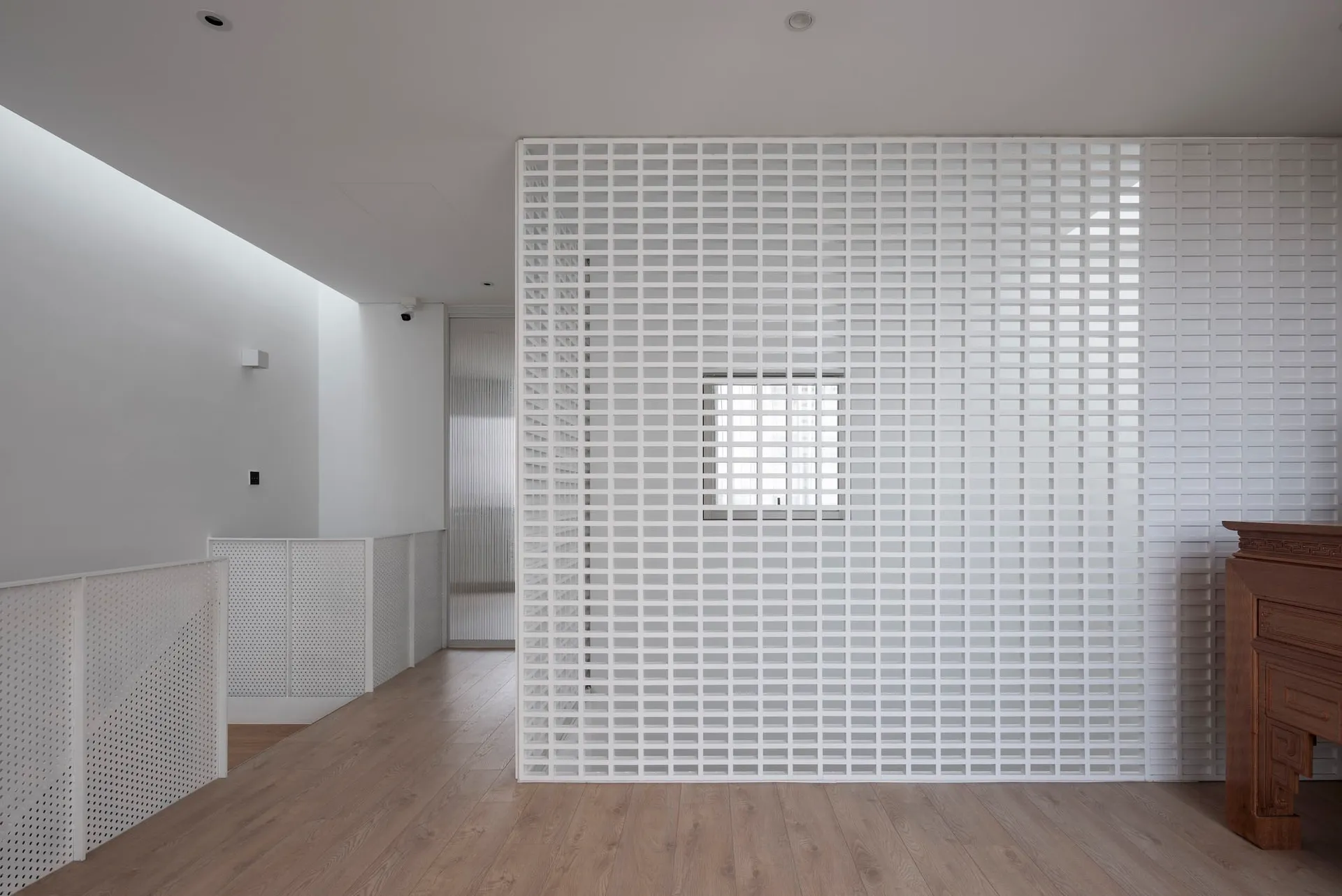 Minimalist white room with grid-patterned walls and ceiling, featuring a wooden floor and a fireplace.