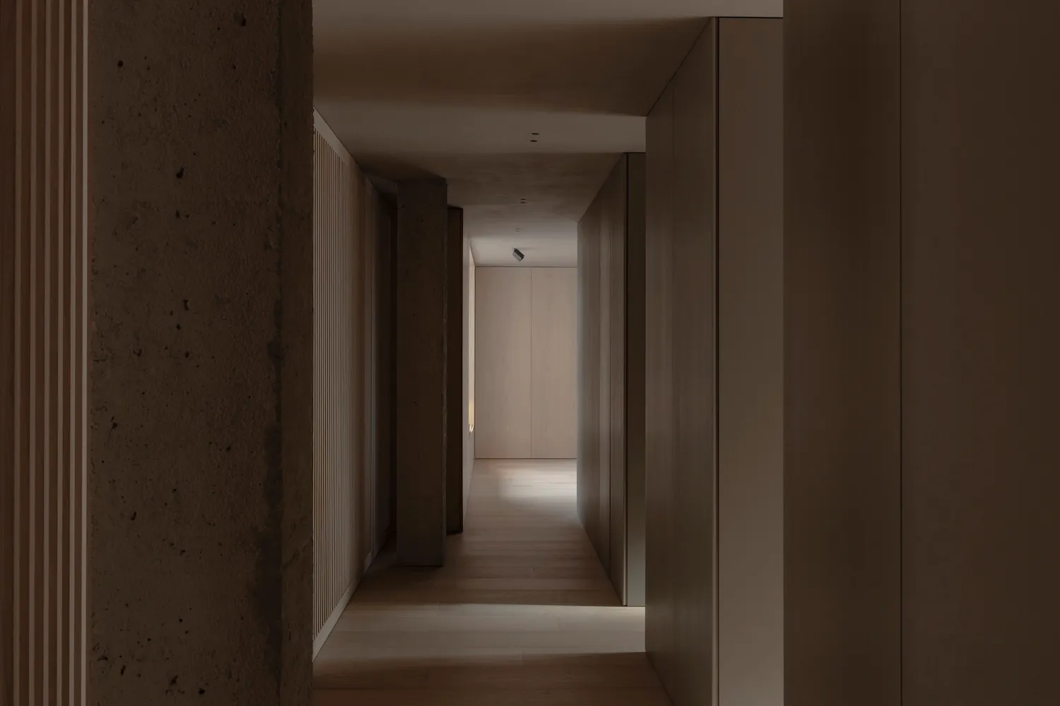 A minimalist hallway with wooden flooring and concrete walls.