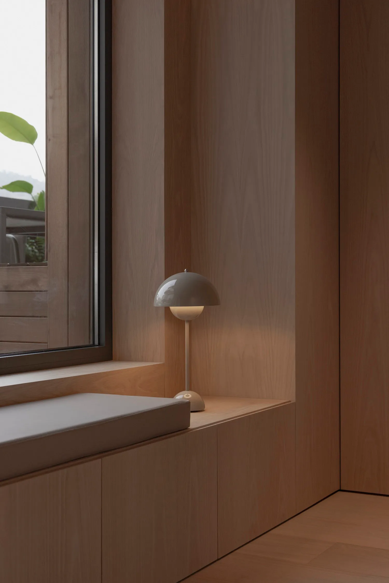 A minimalist window corner featuring wooden paneling and a small lamp.