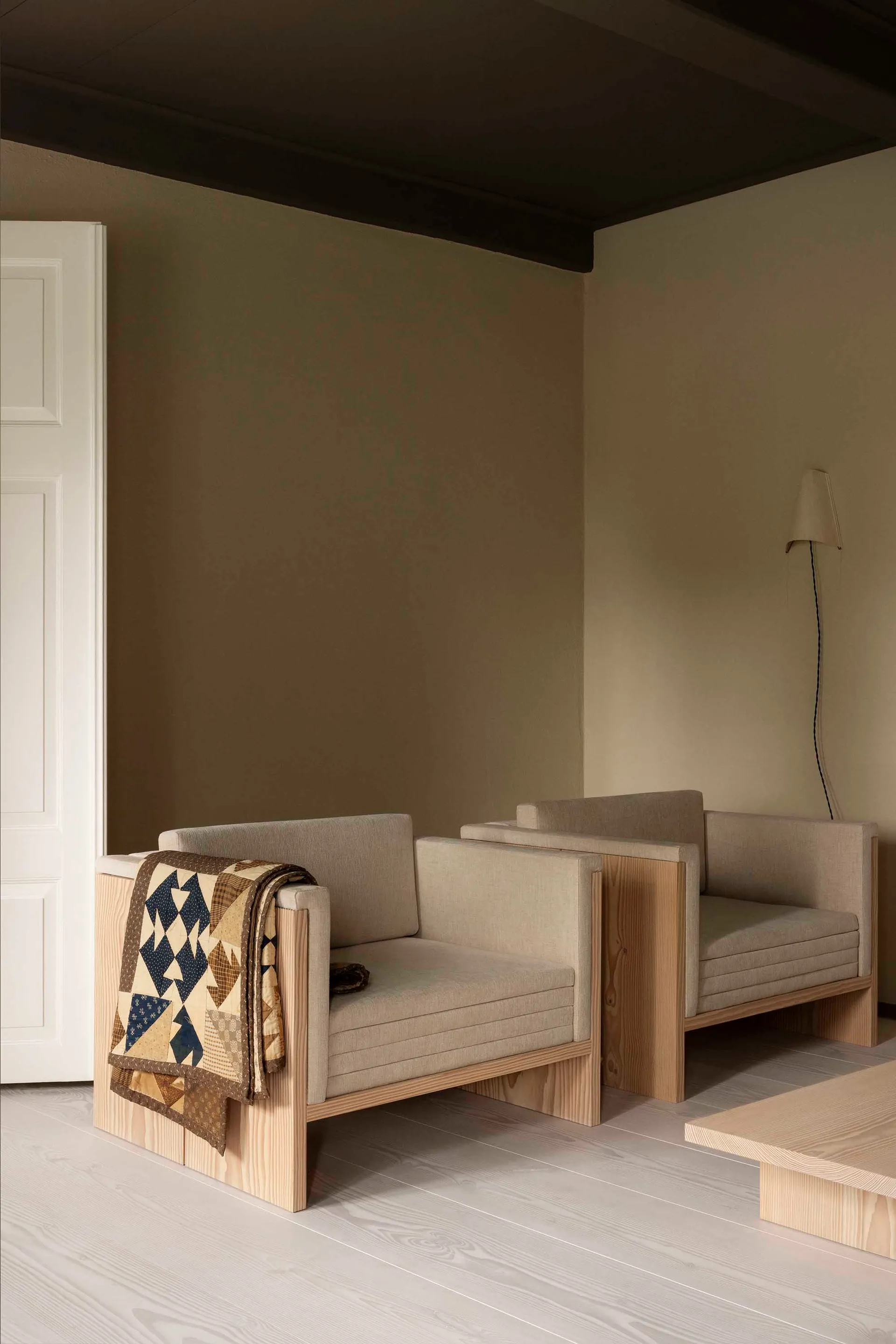 A modern interior featuring wooden furniture with a quilt draped over one of the chairs.