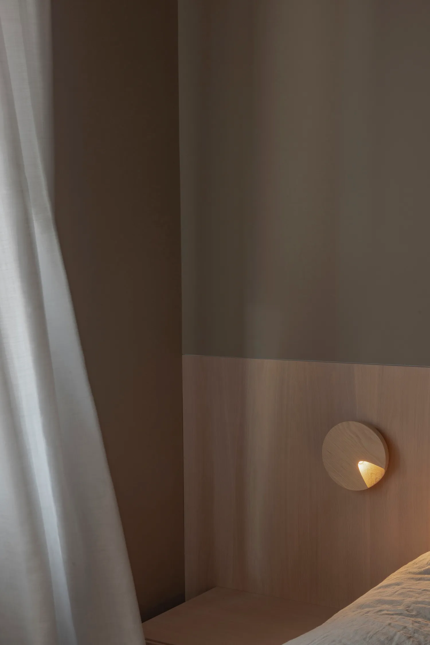 Minimalist bedroom with wooden walls, light fixture, and sheer curtains.