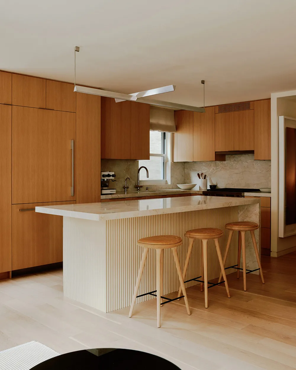 Modern kitchen interior with wood cabinets, marble countertops, and a central island with stools.