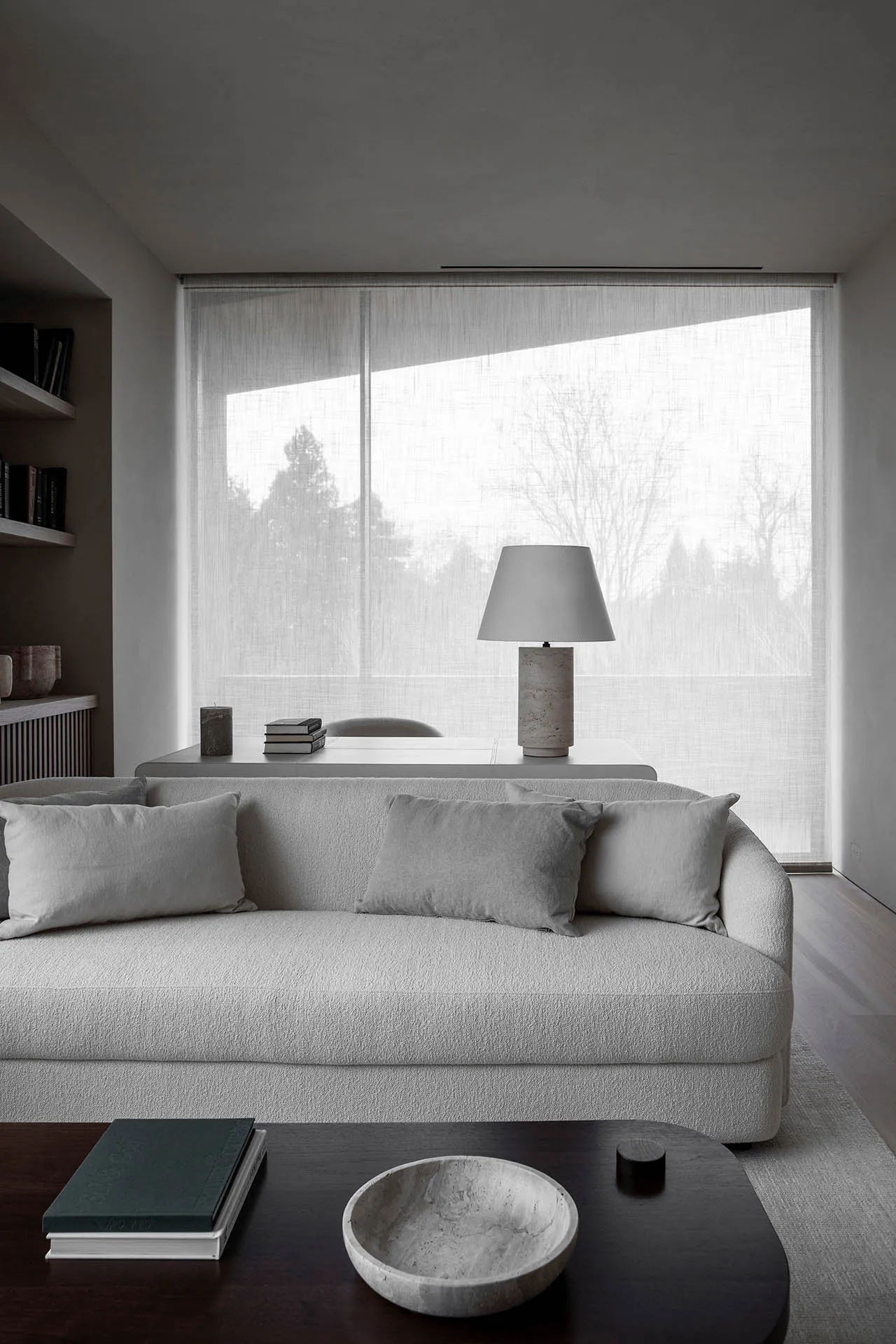 Minimalist living room with a neutral-toned sofa, coffee table, and a large window allowing natural light to fill the space.