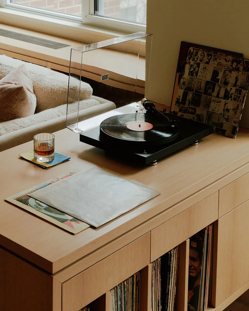 A wooden furniture piece with a record player, records, and a glass of liquid on top.